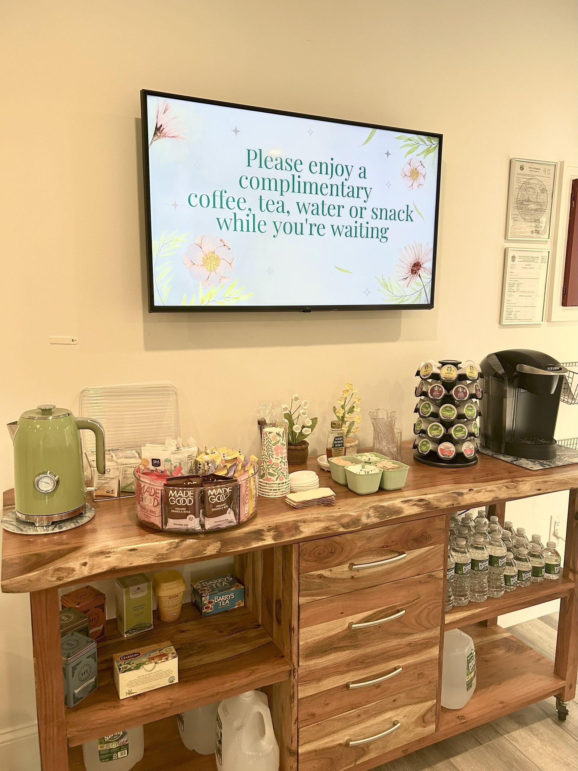 Wooden buffet with coffee station under a TV displaying a message.