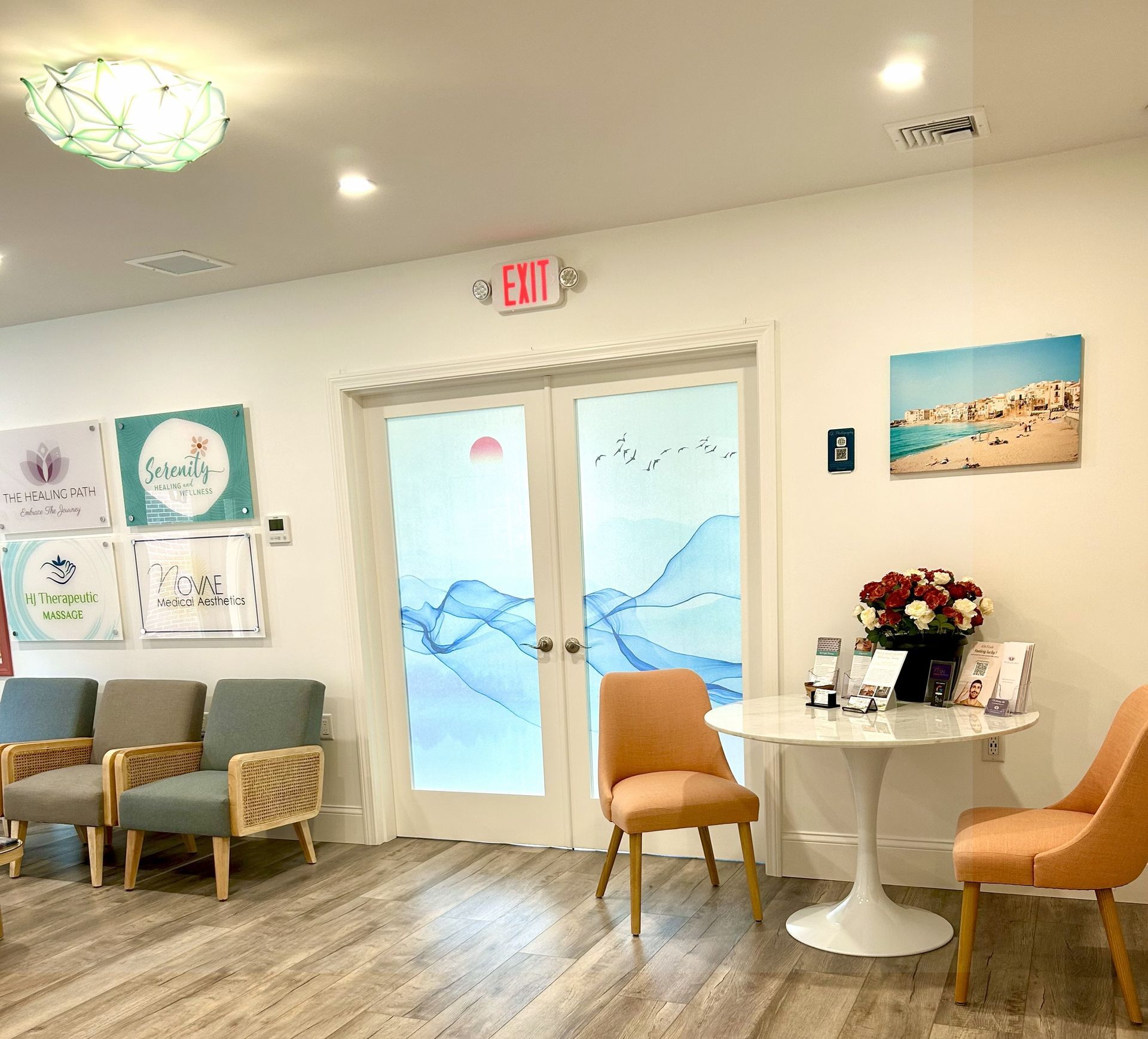 Bright waiting room with tan walls, chairs, and a round table.  Two doors with a blue wave design lead outside.