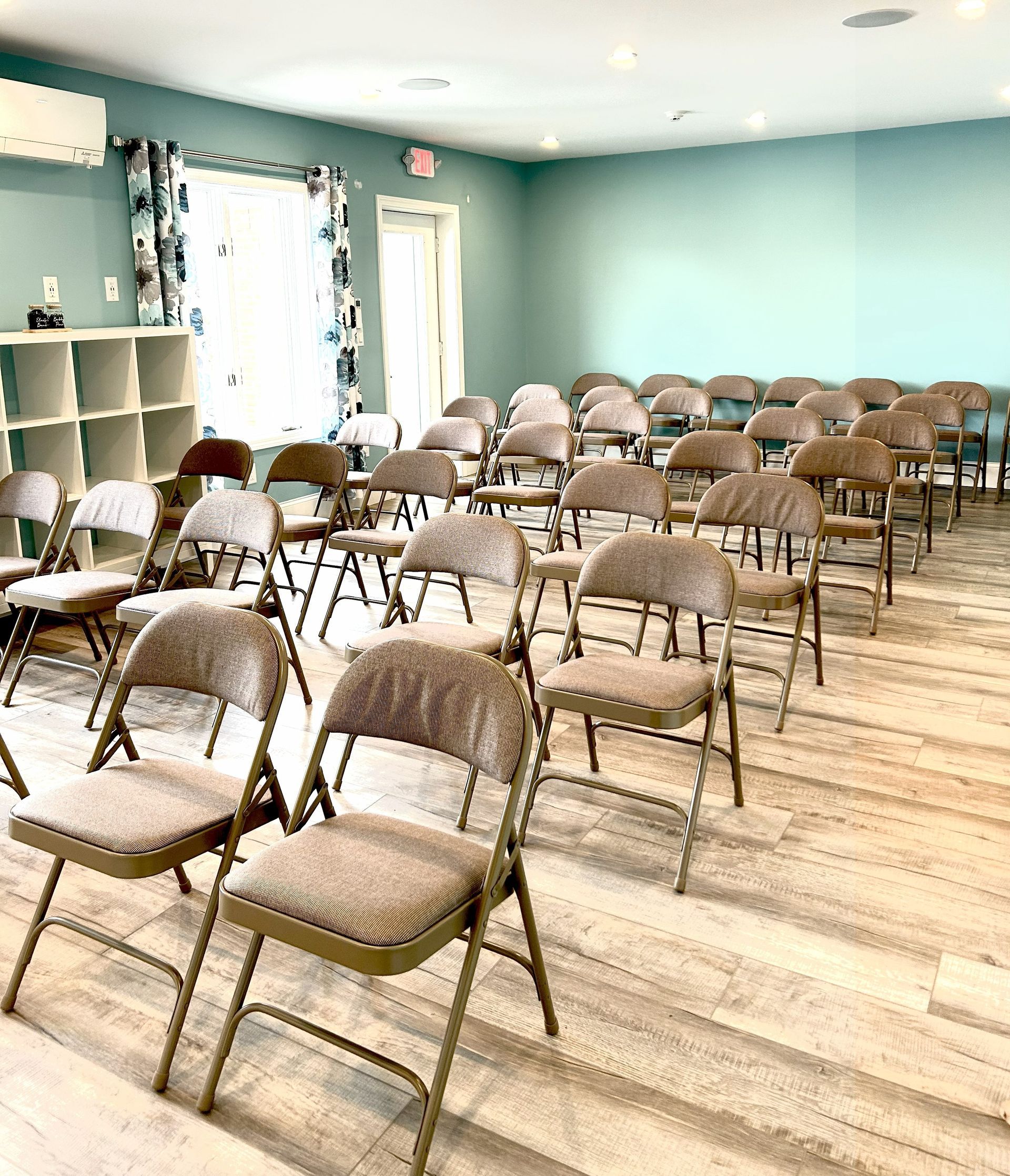 Rows of tan chairs face forward in a brightly lit room with a light blue wall.