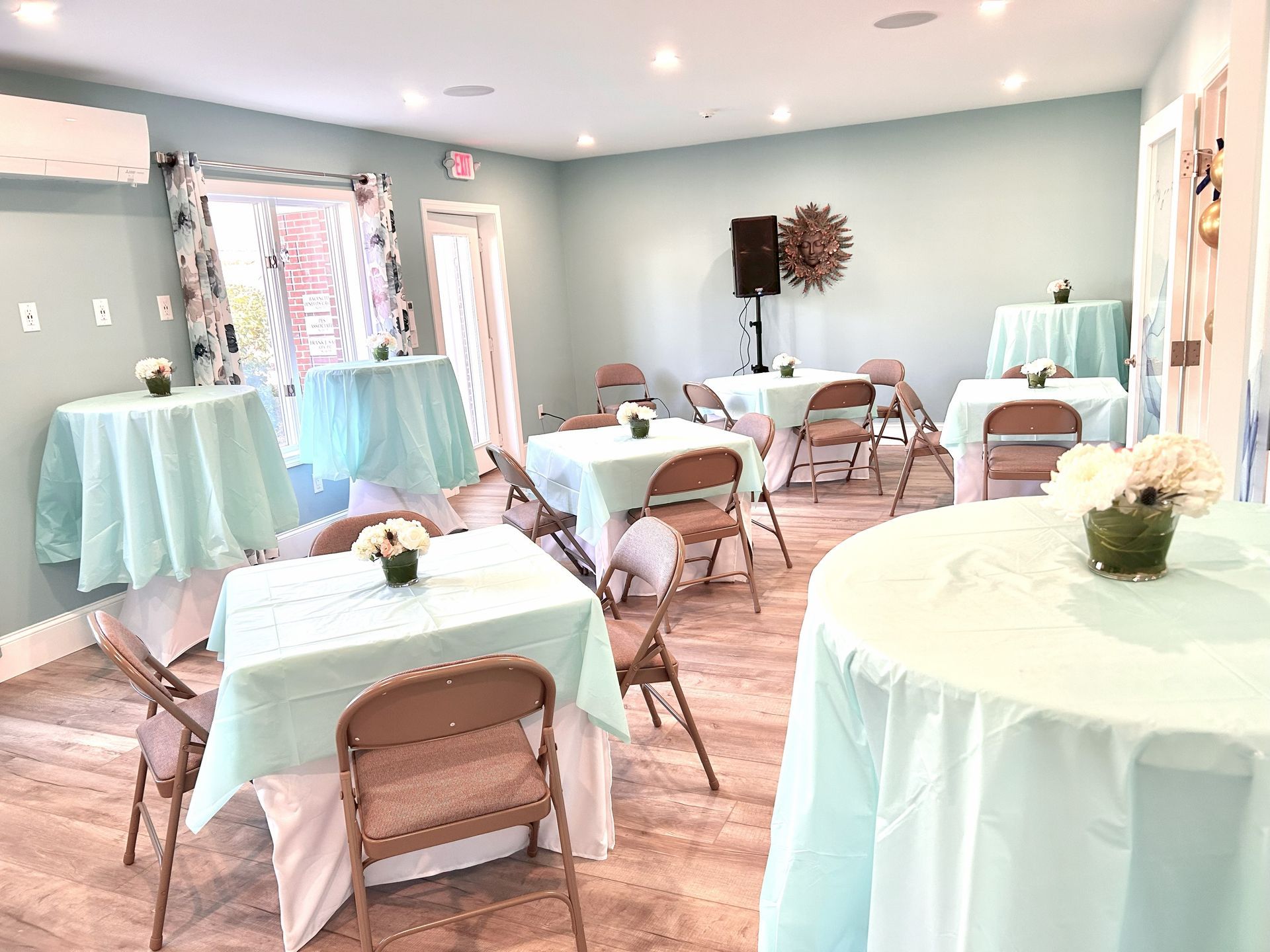 Event room with teal tablecloths, brown chairs, and floral centerpieces.