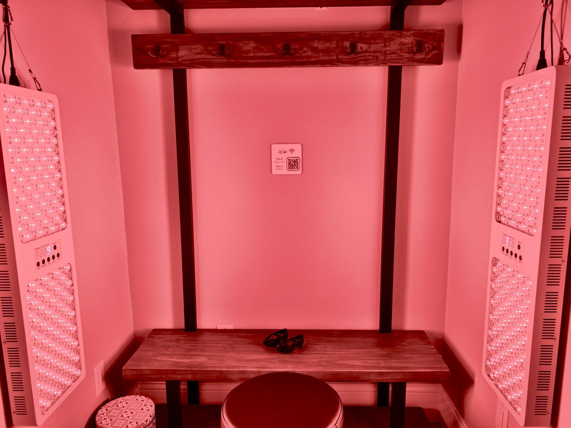 Red-toned room with a wooden table, stool, and two LED light panels flanking a centered wall.