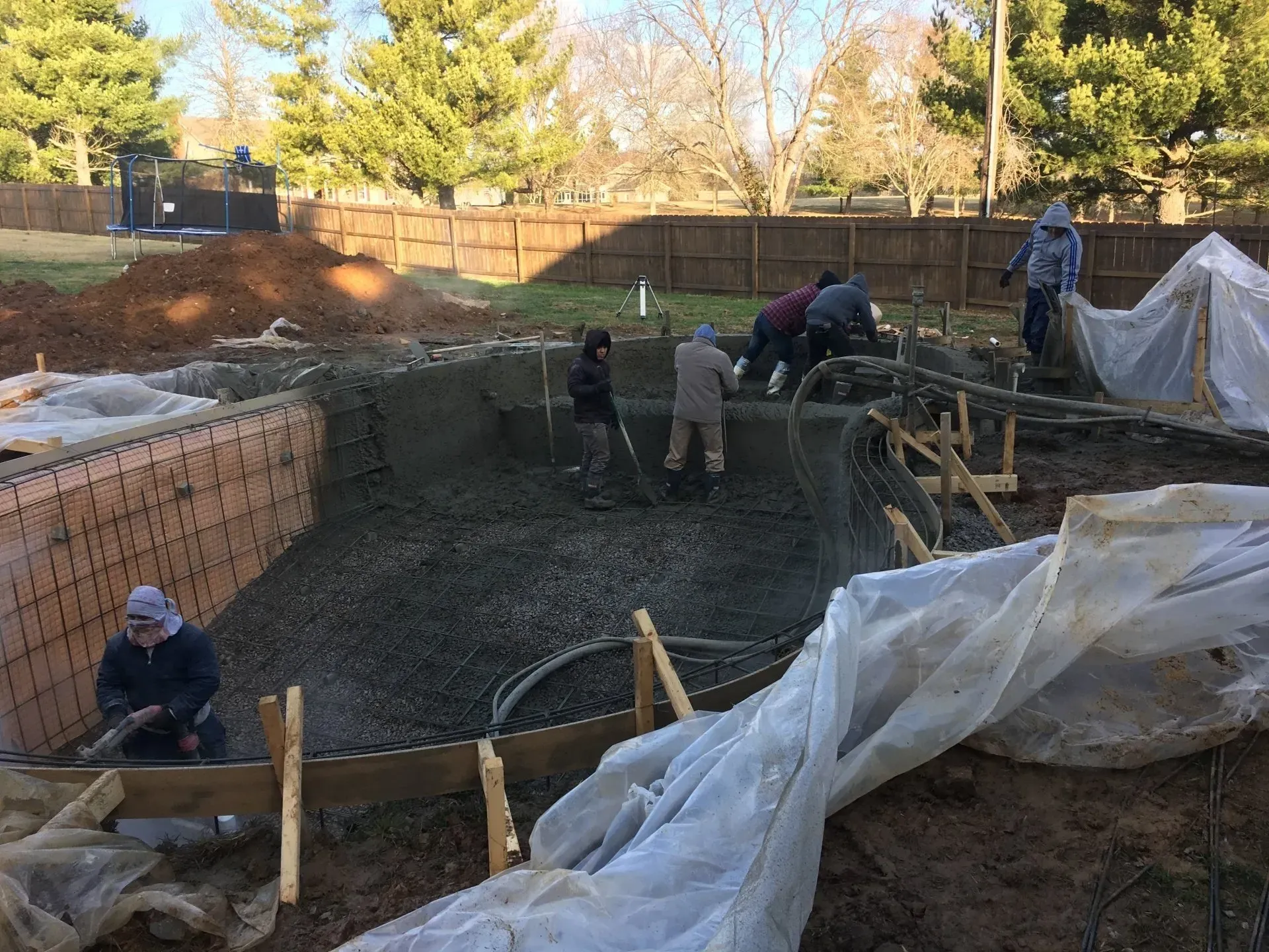 Construction of a pool. Workers using tools, pouring concrete. Brick walls surround the excavation.