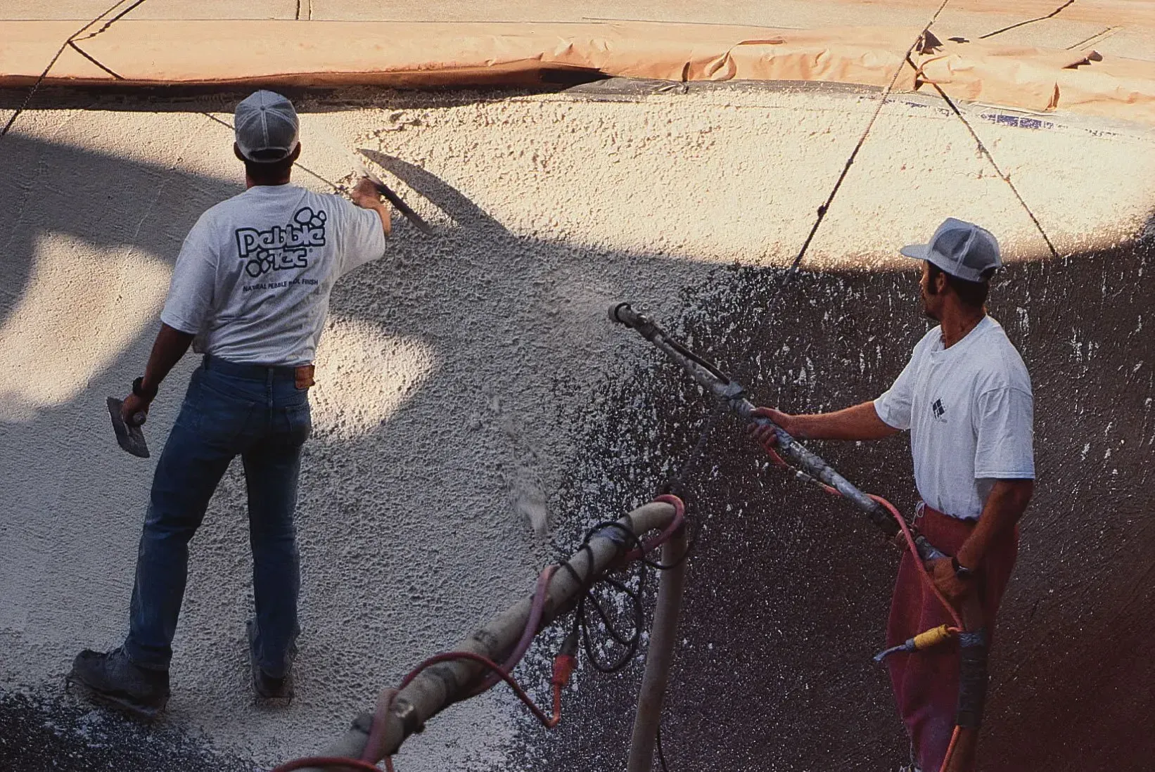 Two construction workers applying a concrete coating with a spray gun on a wall.
