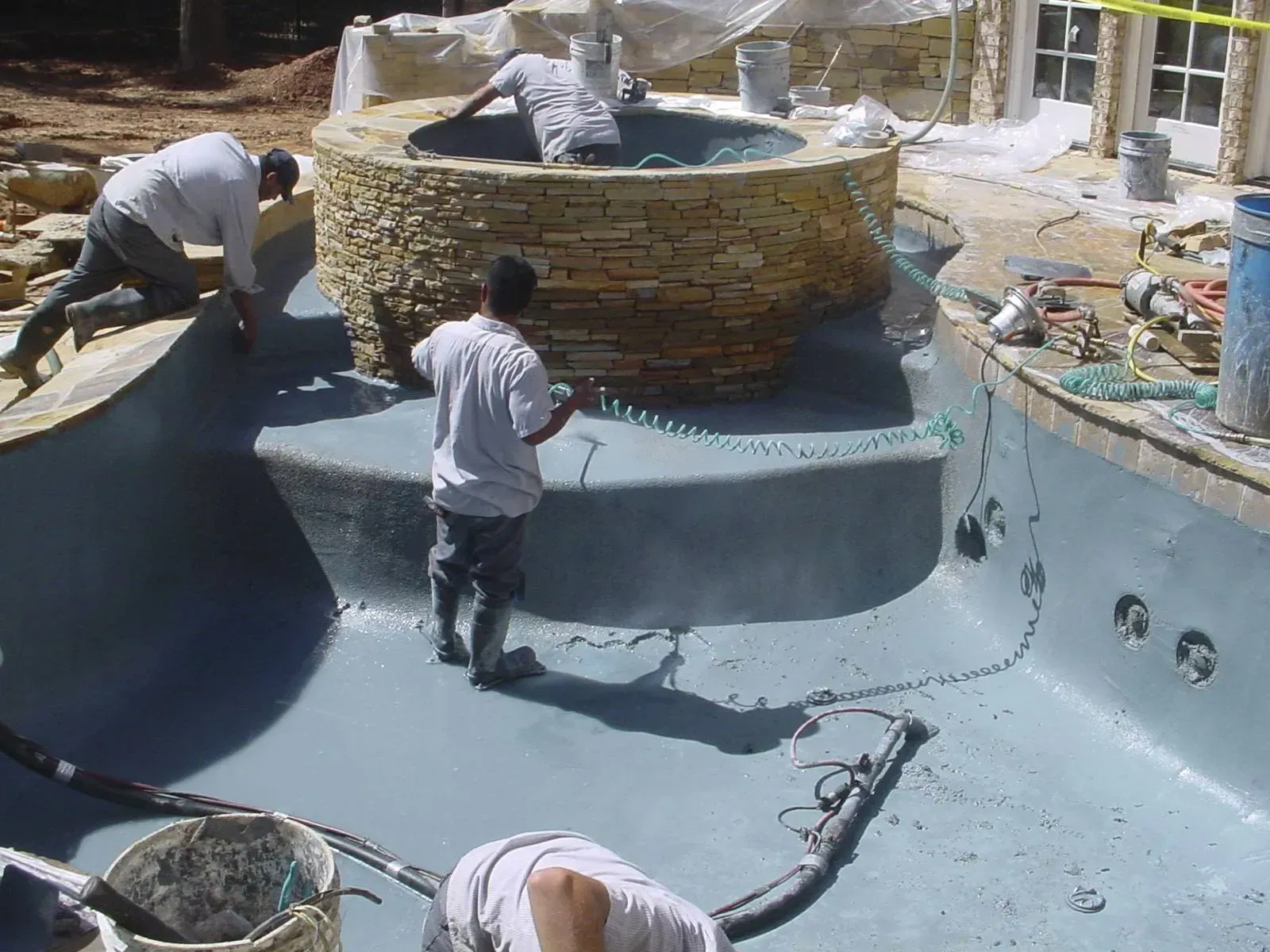 Construction workers apply material to a pool and spa. Brown stone surround and light blue interior.