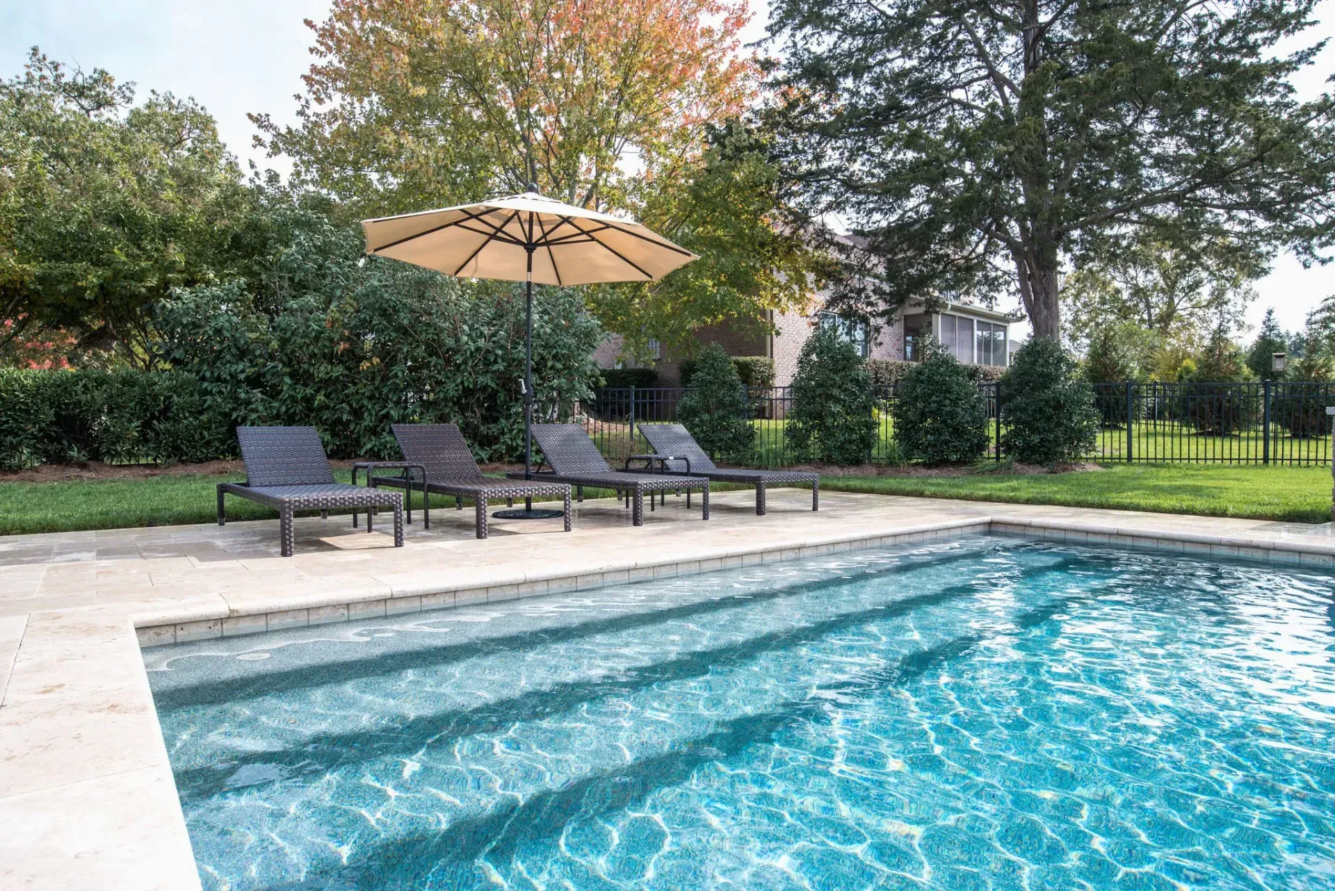 Pool with chaise lounges, umbrella, and lush greenery in a backyard setting.