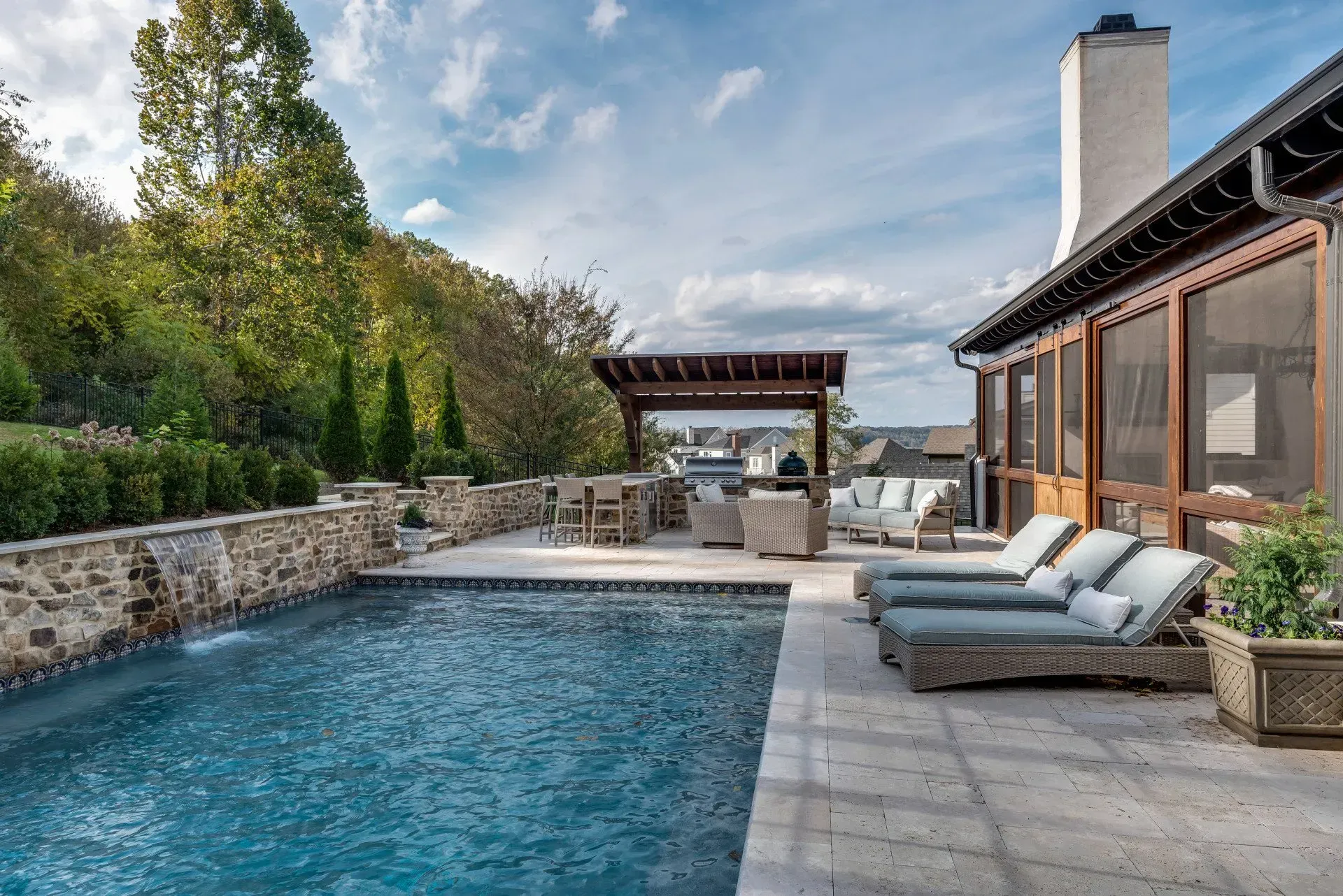 Swimming pool with stone wall and water feature, outdoor seating, and house.