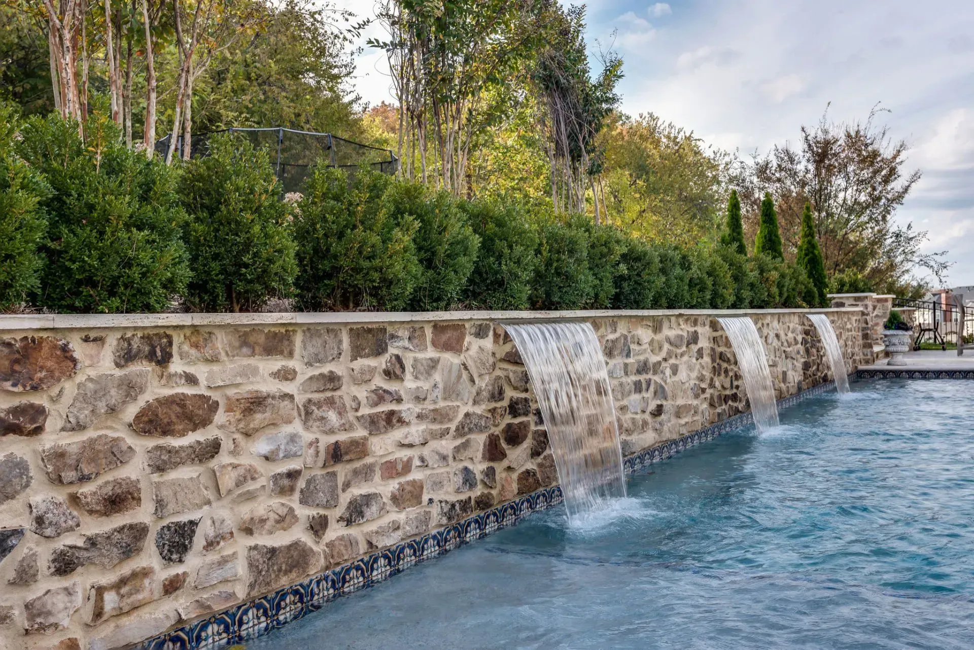 Stone wall with cascading waterfalls into a swimming pool, lush greenery in the background.
