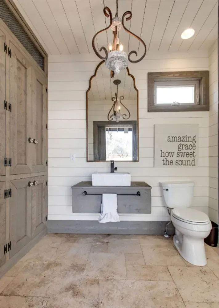 Rustic bathroom with a vanity, toilet, and ornate mirror. Includes a light fixture and cabinets.