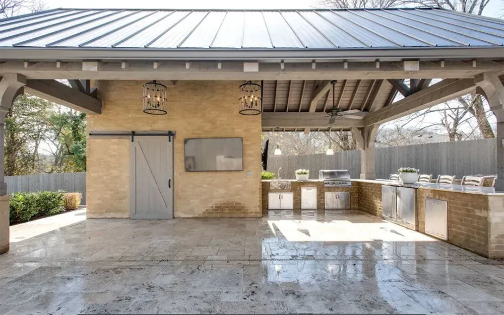 Outdoor kitchen under a gray roof, featuring a stone-covered bar, stainless steel appliances, and a sliding barn door.