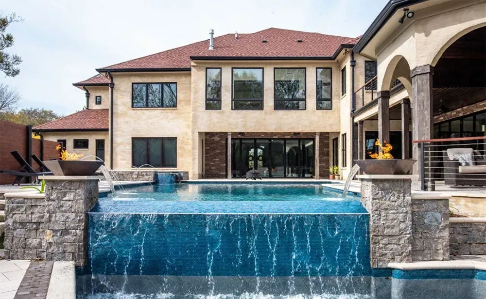 Luxury home with pool; water cascades over the edge into a shallow pool.
