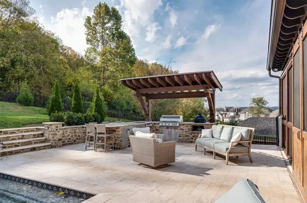 Patio with outdoor kitchen, seating area, pergola, and hill in the background.