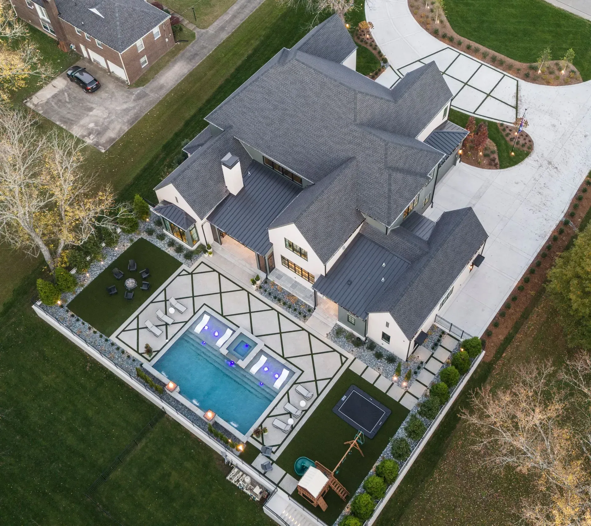 Aerial view of a large modern home with a pool, landscaping, and a long driveway.