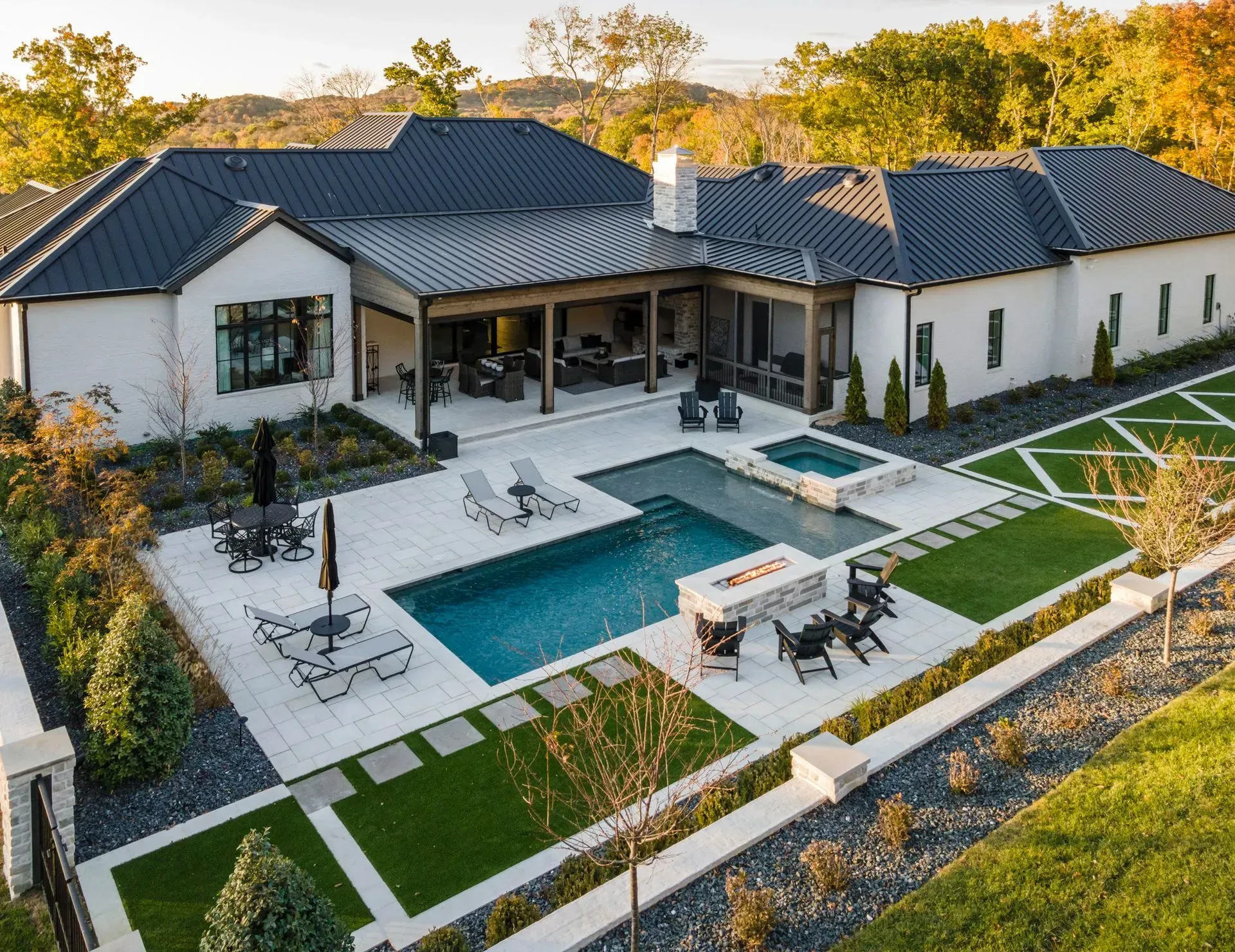 Modern white house with pool, patio, and black metal roof in a sunny setting.