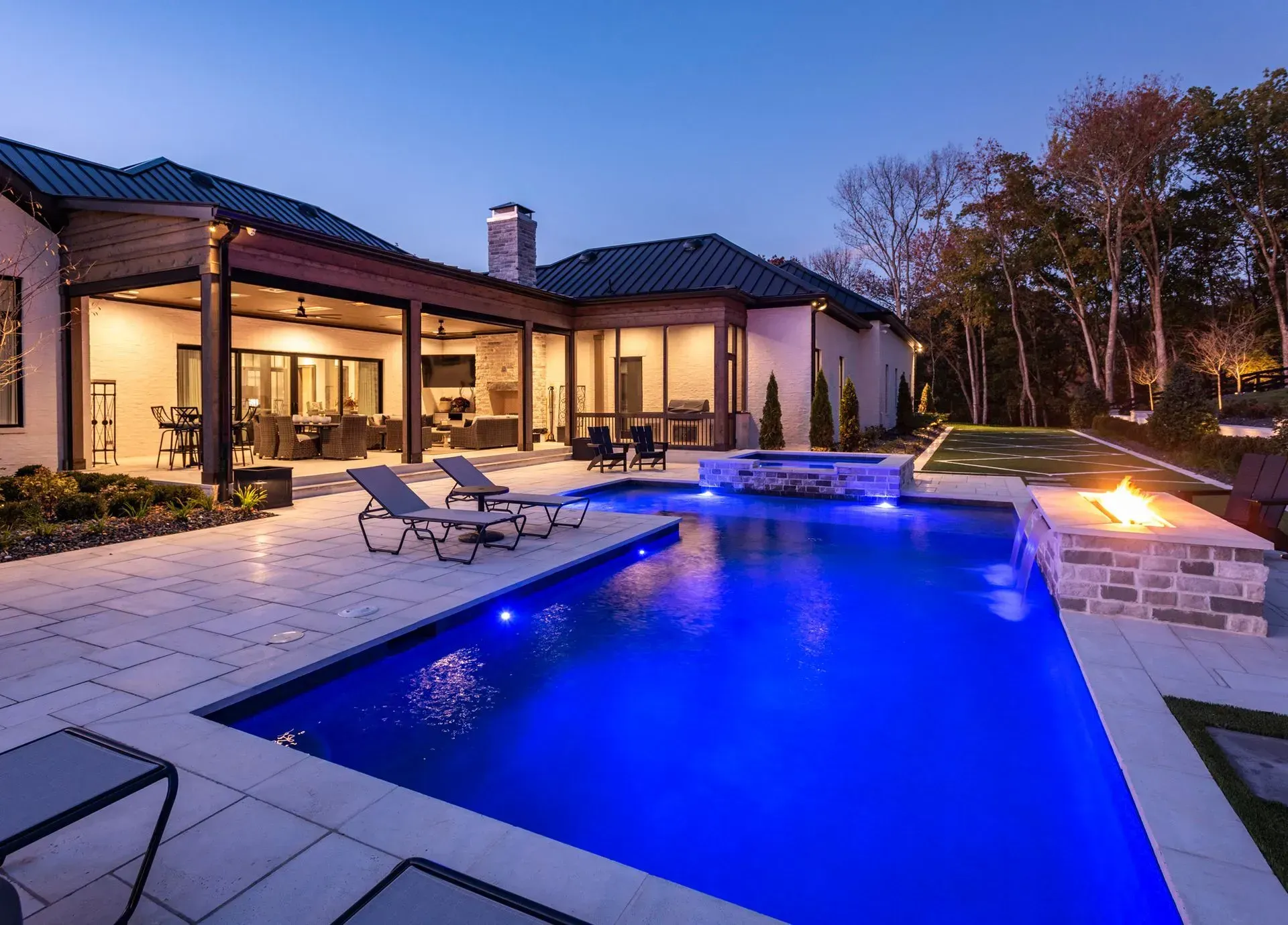 Luxury backyard pool with blue water, lounge chairs, fire pit, and a modern home.