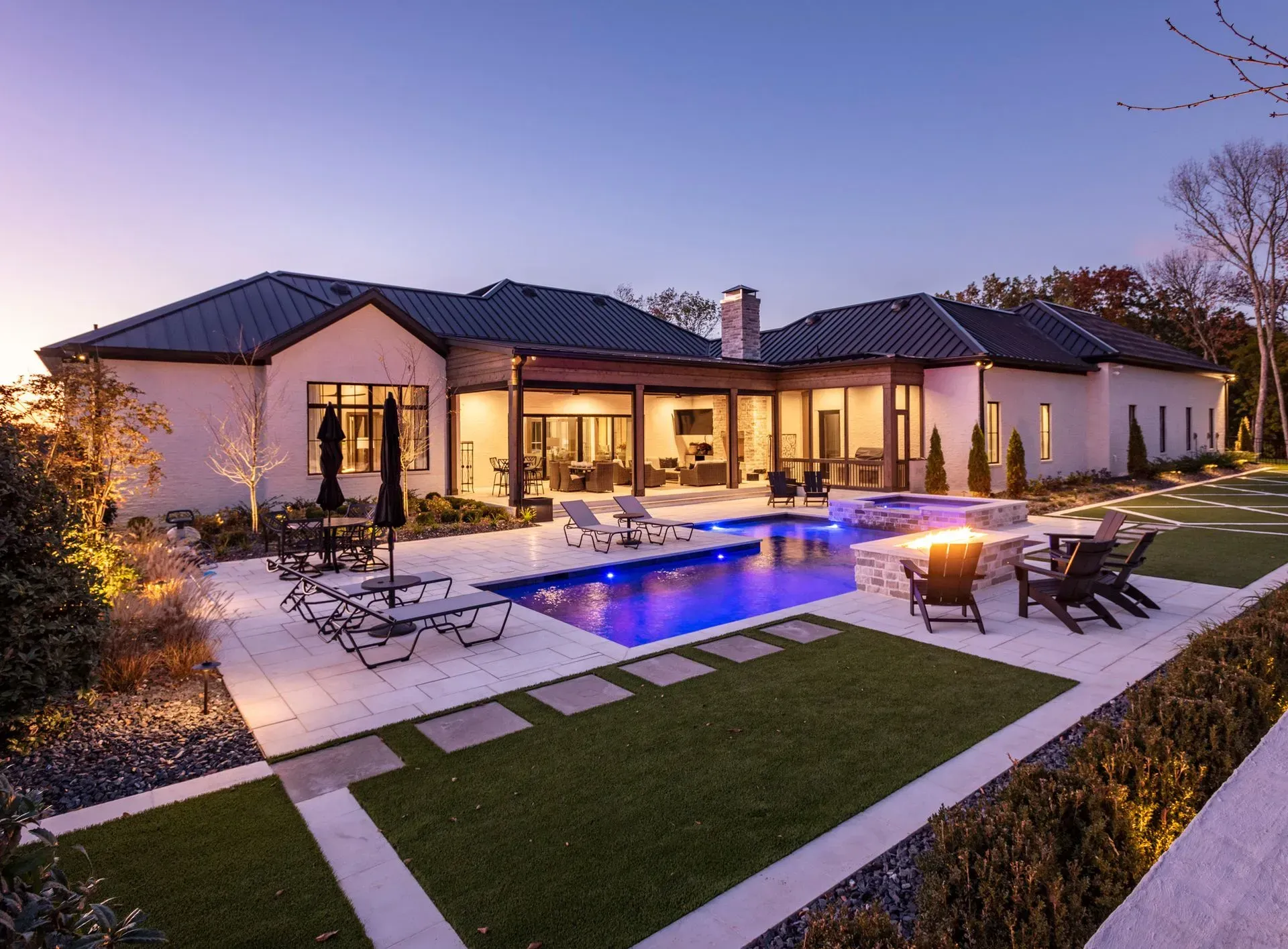 Luxury home with pool, patio, and outdoor fireplace. Evening setting, dark blue pool, and lounge chairs.