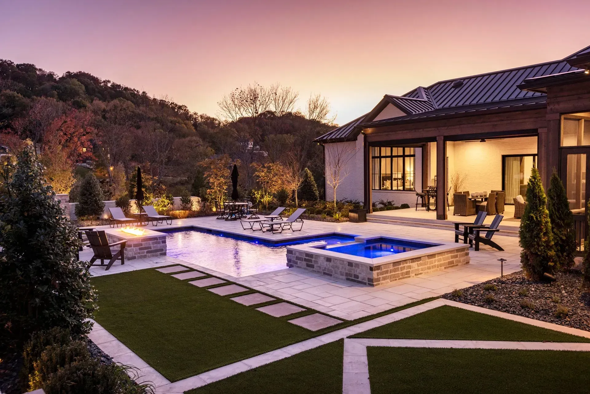 Backyard with pool, spa, and patio at dusk; illuminated with soft lighting.