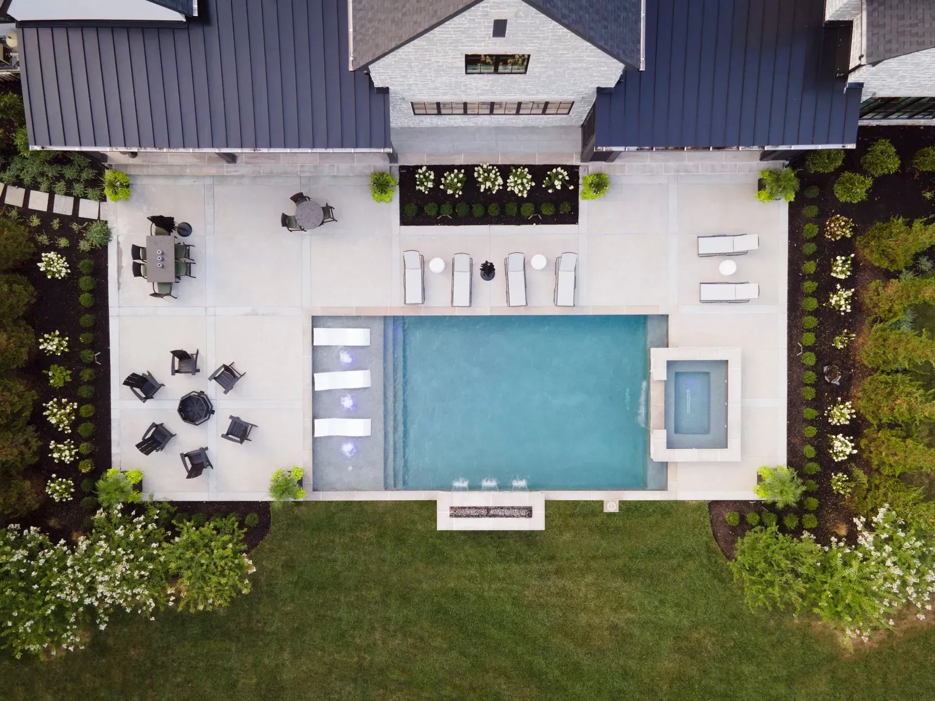 Overhead view of a luxury backyard with a pool, patio, seating areas, and landscaped lawn.