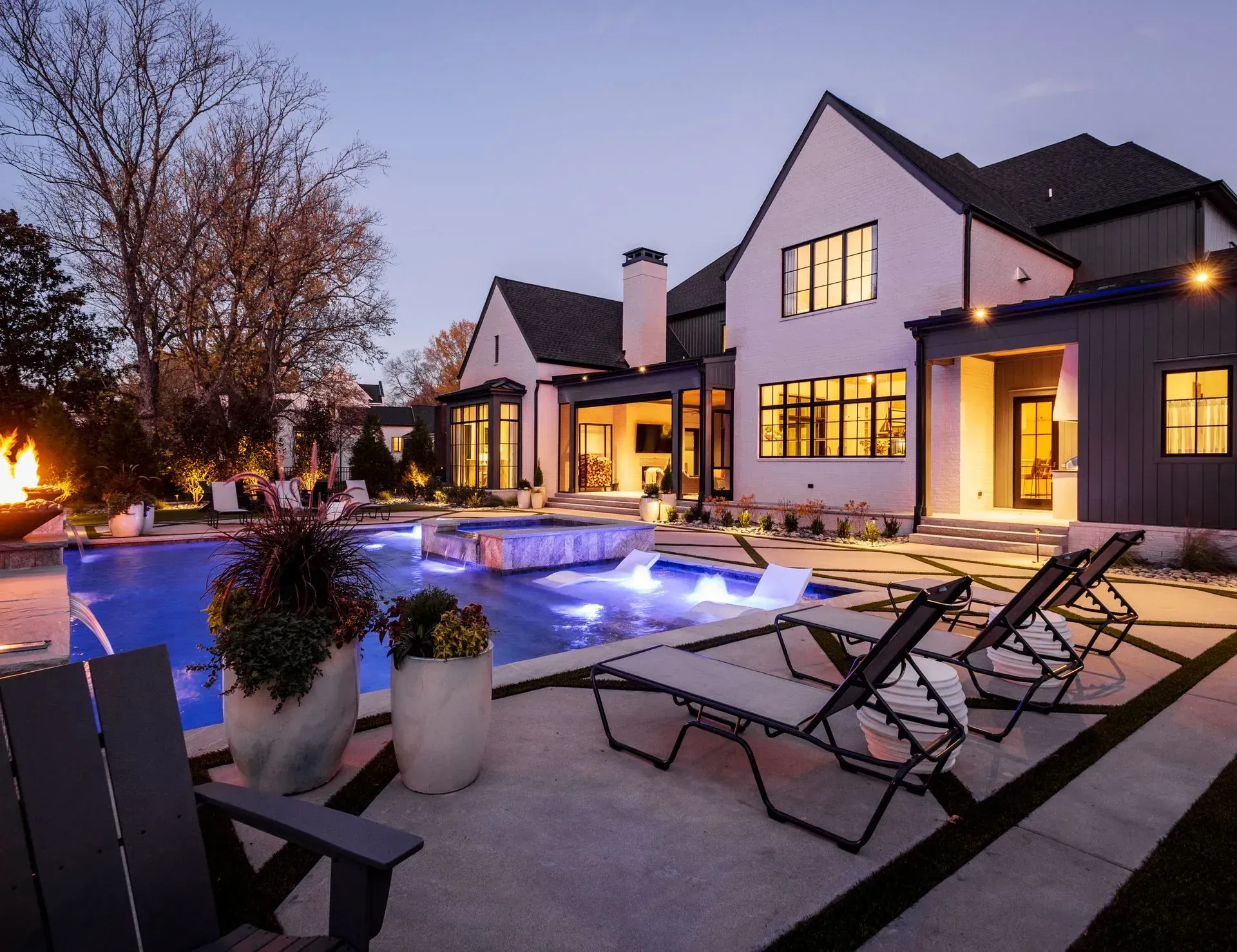 Luxury home exterior with illuminated pool and lounge chairs at dusk.