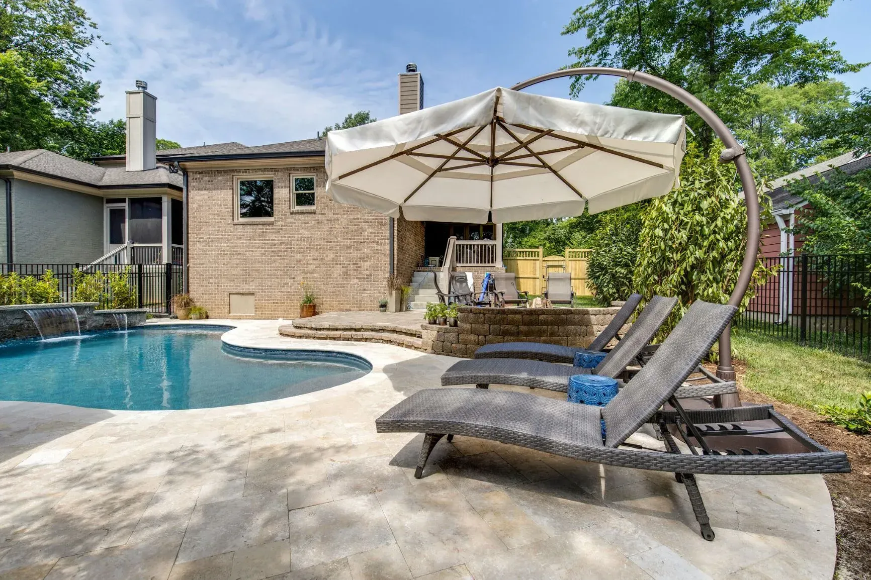 Swimming pool with lounge chairs under a large umbrella in a backyard setting.