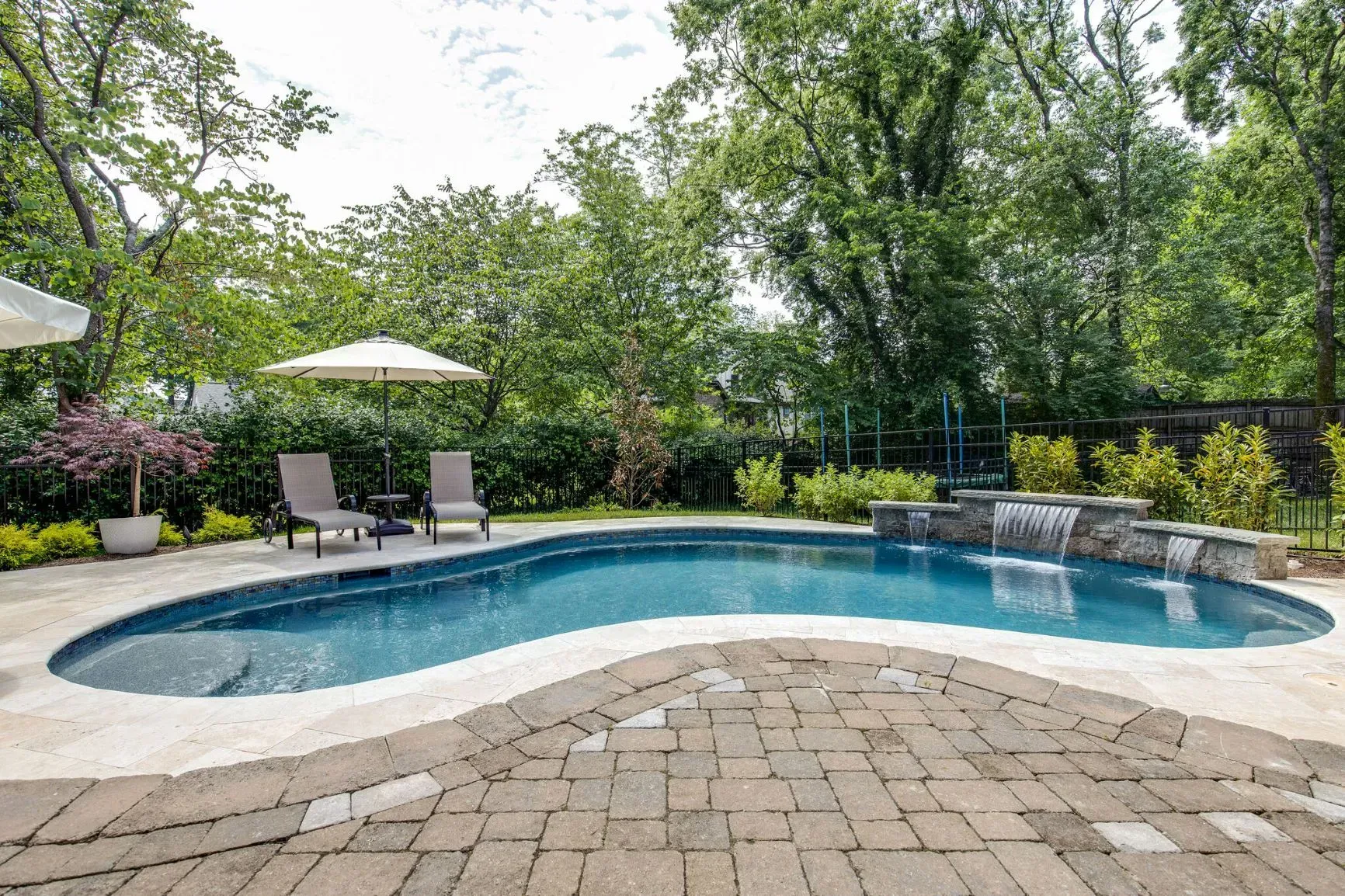 Pool and patio area with lounge chairs, umbrella, and waterfall feature.