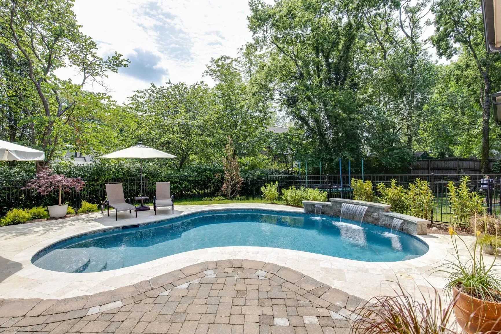 Backyard with a swimming pool, waterfall feature, patio furniture, and lush greenery.
