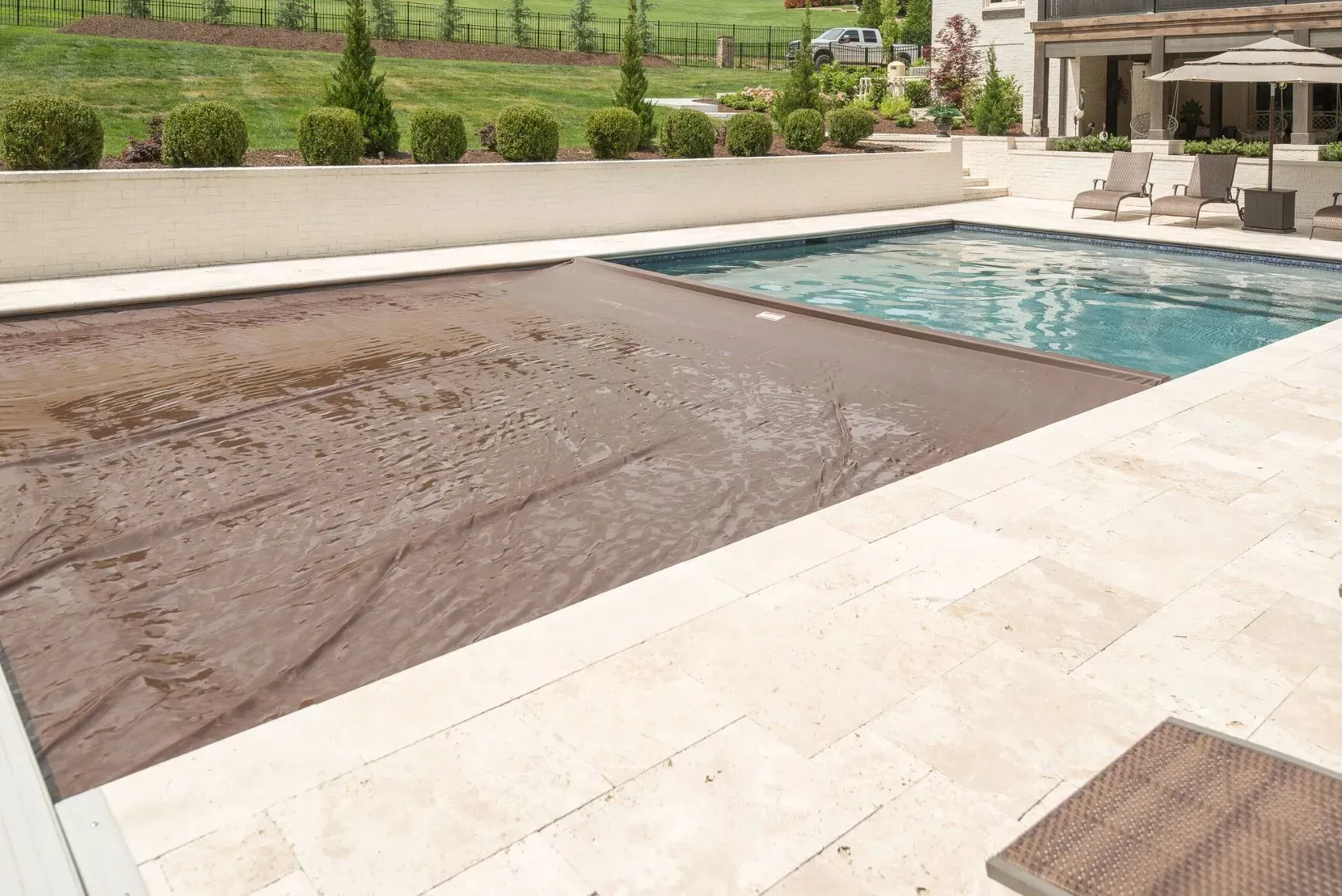Pool with a brown cover partially covering the water, surrounded by light-colored stone patio.