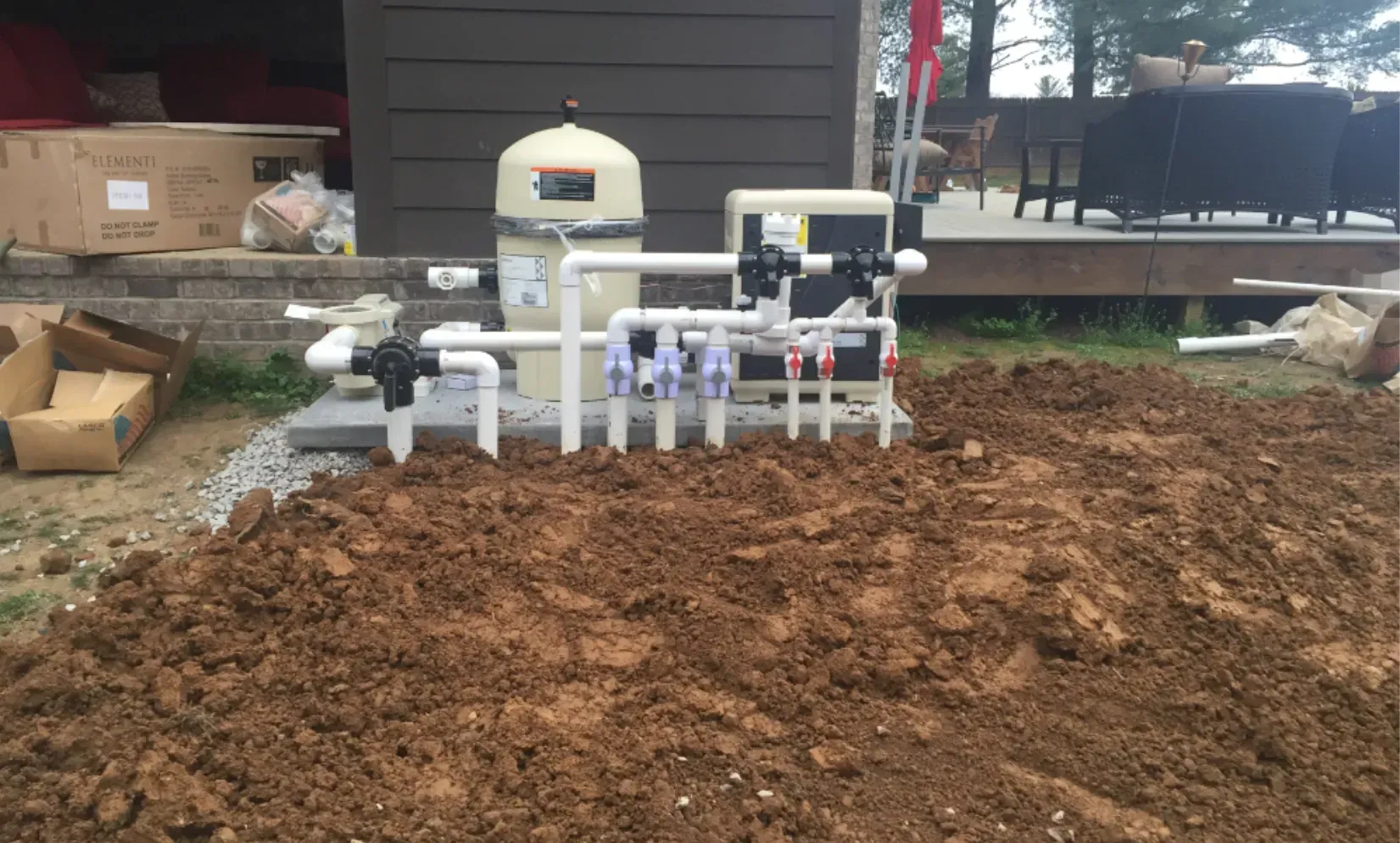 Pool equipment installed on a concrete pad with dirt in front. Beige filter, pipes, and controls.