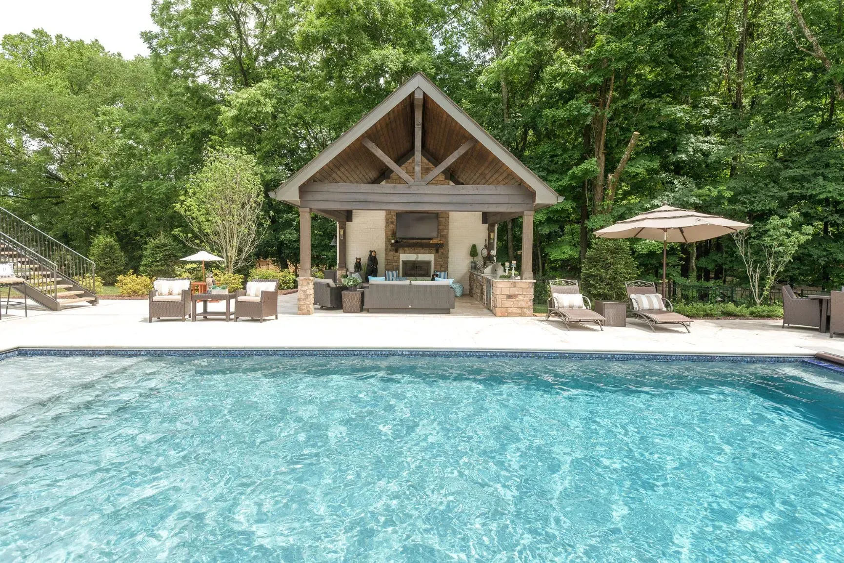 Poolside lounge with a shaded structure, outdoor seating, and trees.