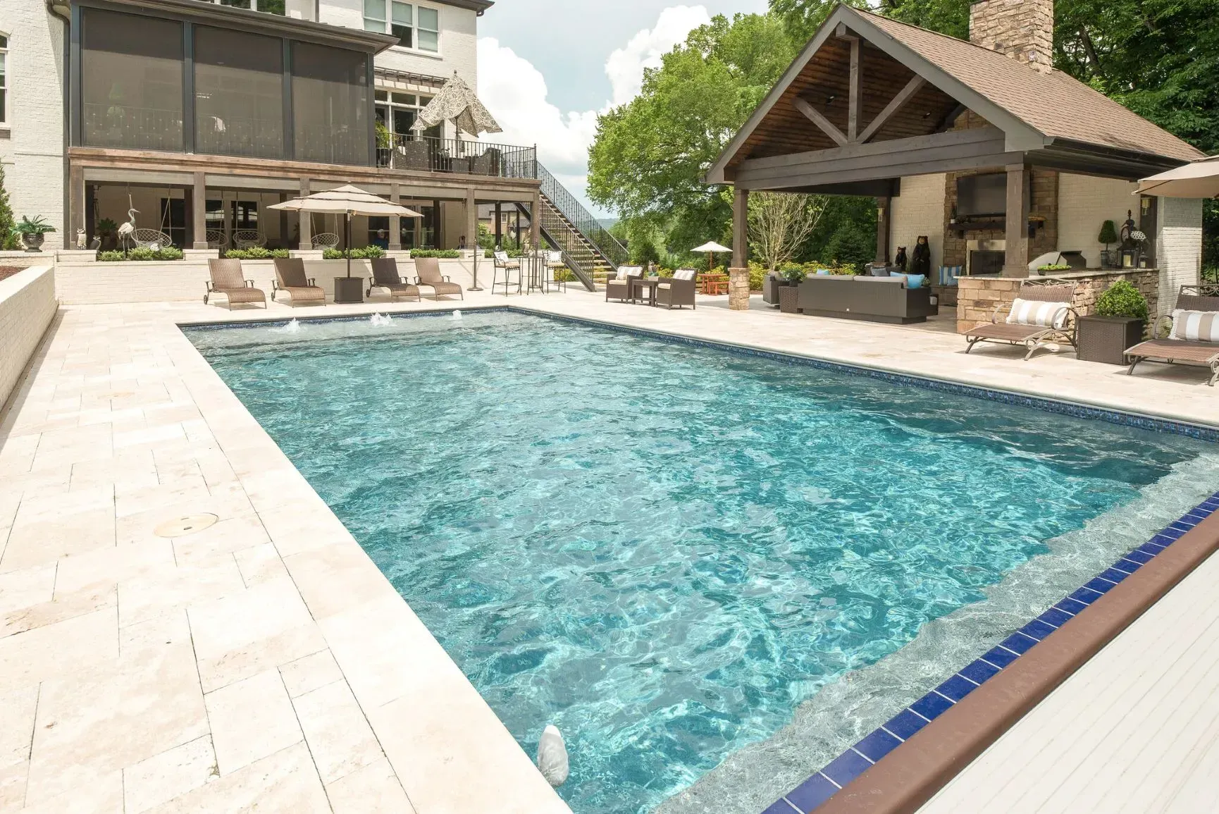 Pool area with a turquoise pool, lounge chairs, and a covered outdoor kitchen.