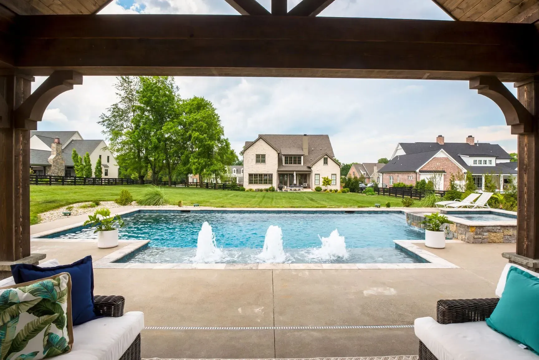 Outdoor patio with pool, fountains, and houses in the background. Turquoise and blue cushions on the seats.