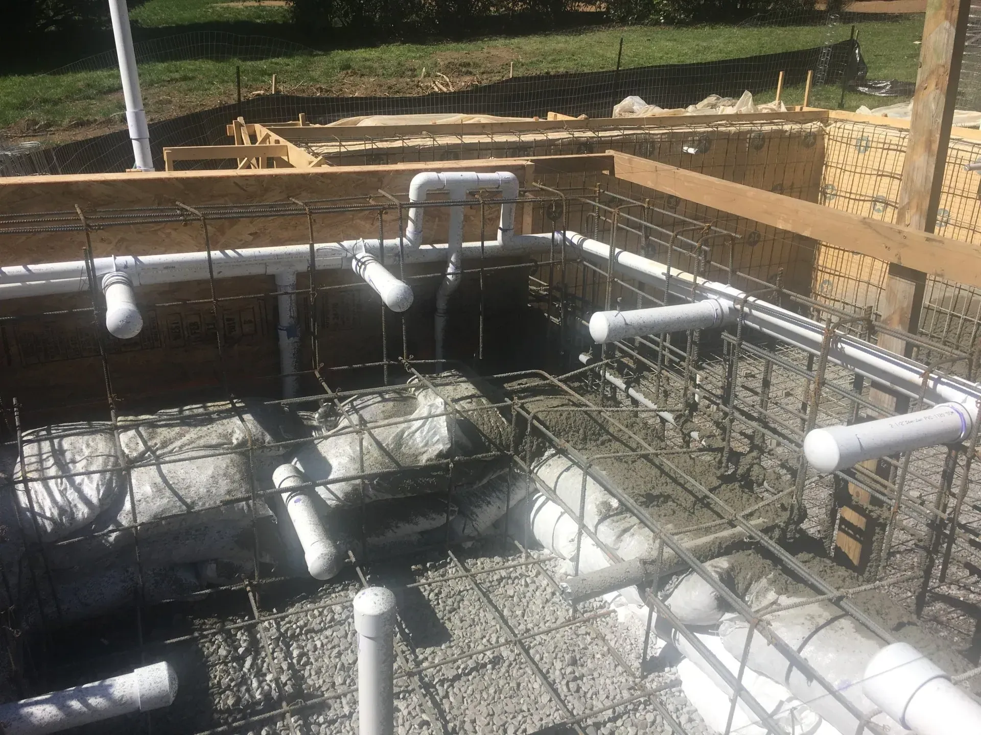 Construction site: concrete form with pipes and rebar framework for a pool or water feature.