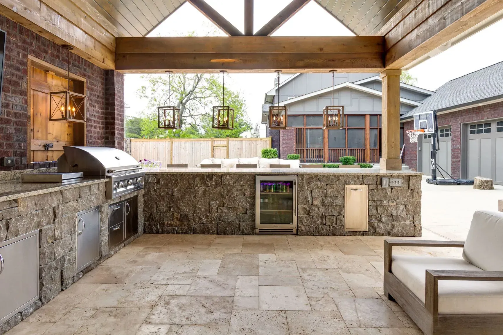 Outdoor kitchen with stone countertops, grill, and seating under a wooden pergola.