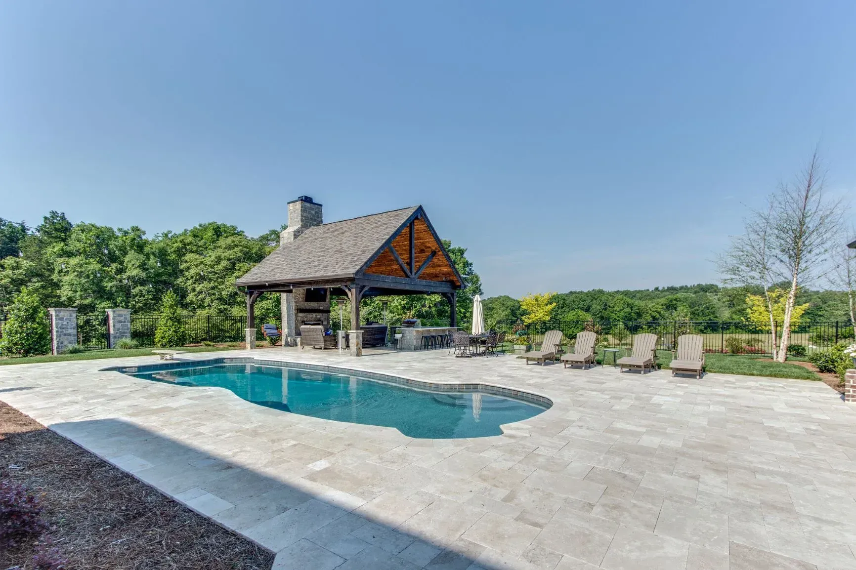 Swimming pool with a covered outdoor kitchen and lounge chairs under a bright blue sky.