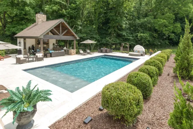 Luxurious outdoor pool area with cabana, trees, and manicured landscaping.