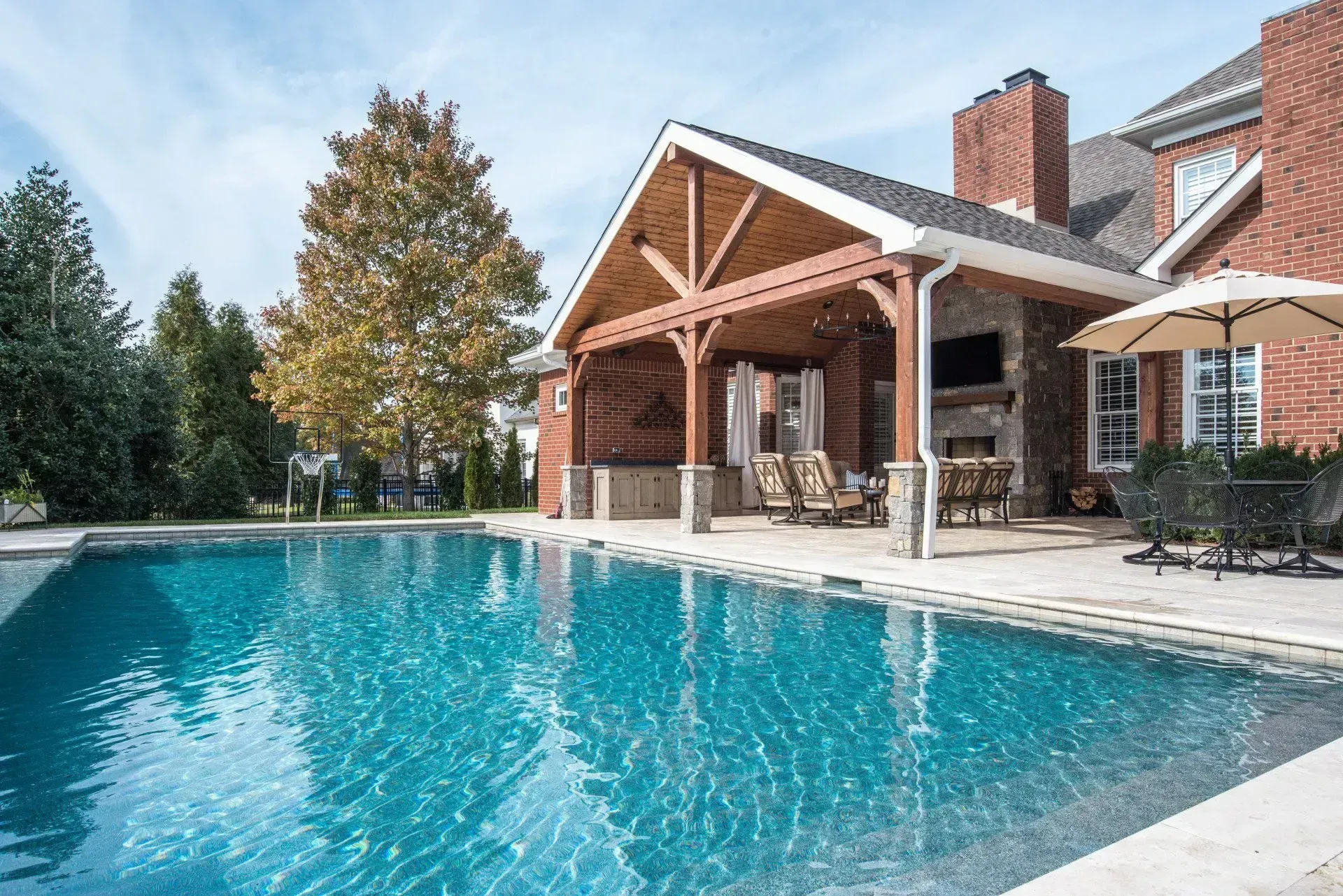 Backyard with a pool, covered patio, brick house, and umbrella.