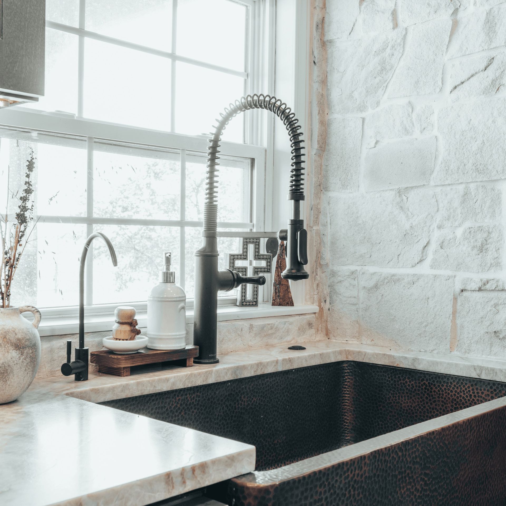 A kitchen sink with a faucet and a window in the background.
