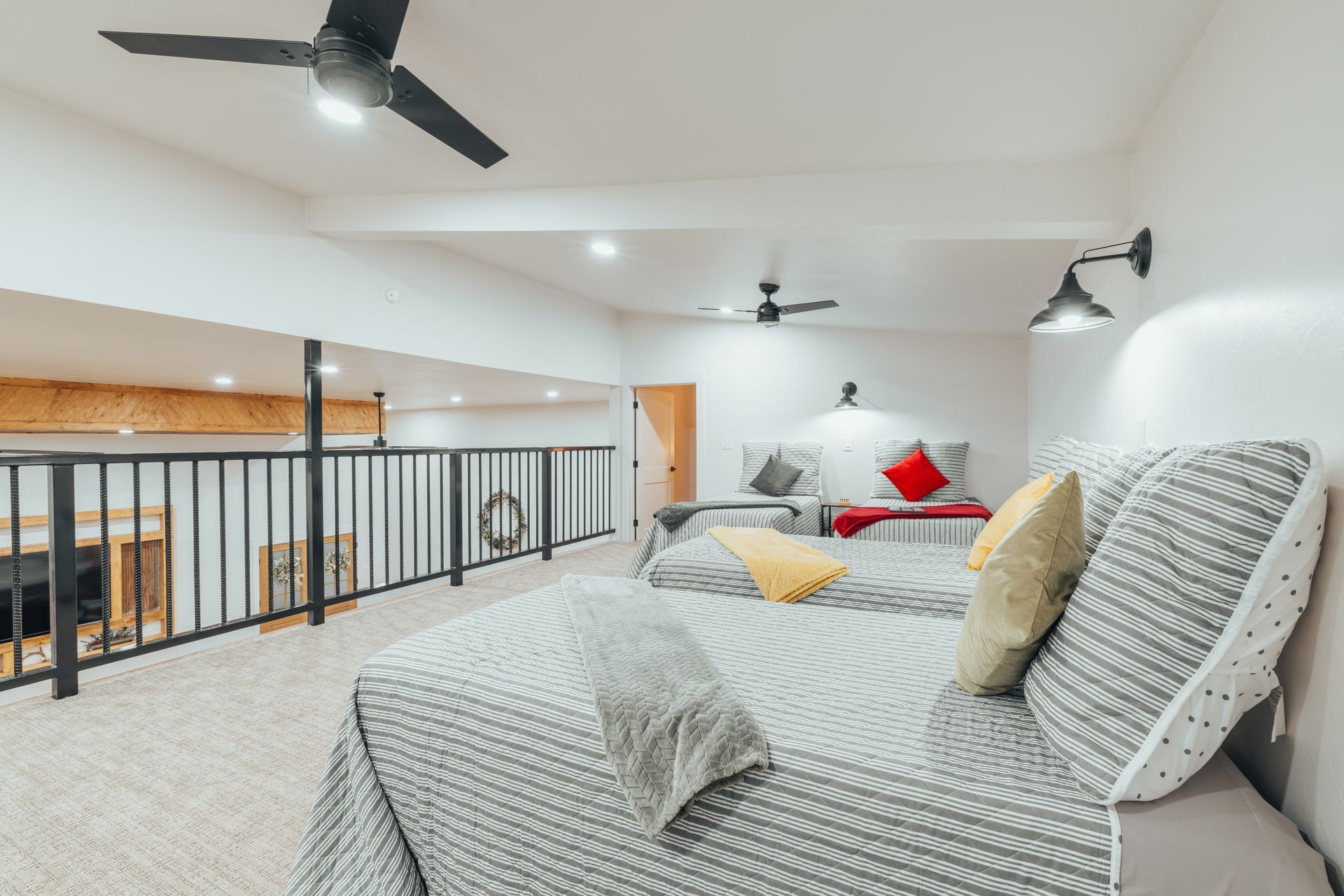 Loft bedroom with beds, a railing, and overhead fans. White walls and a neutral carpet.