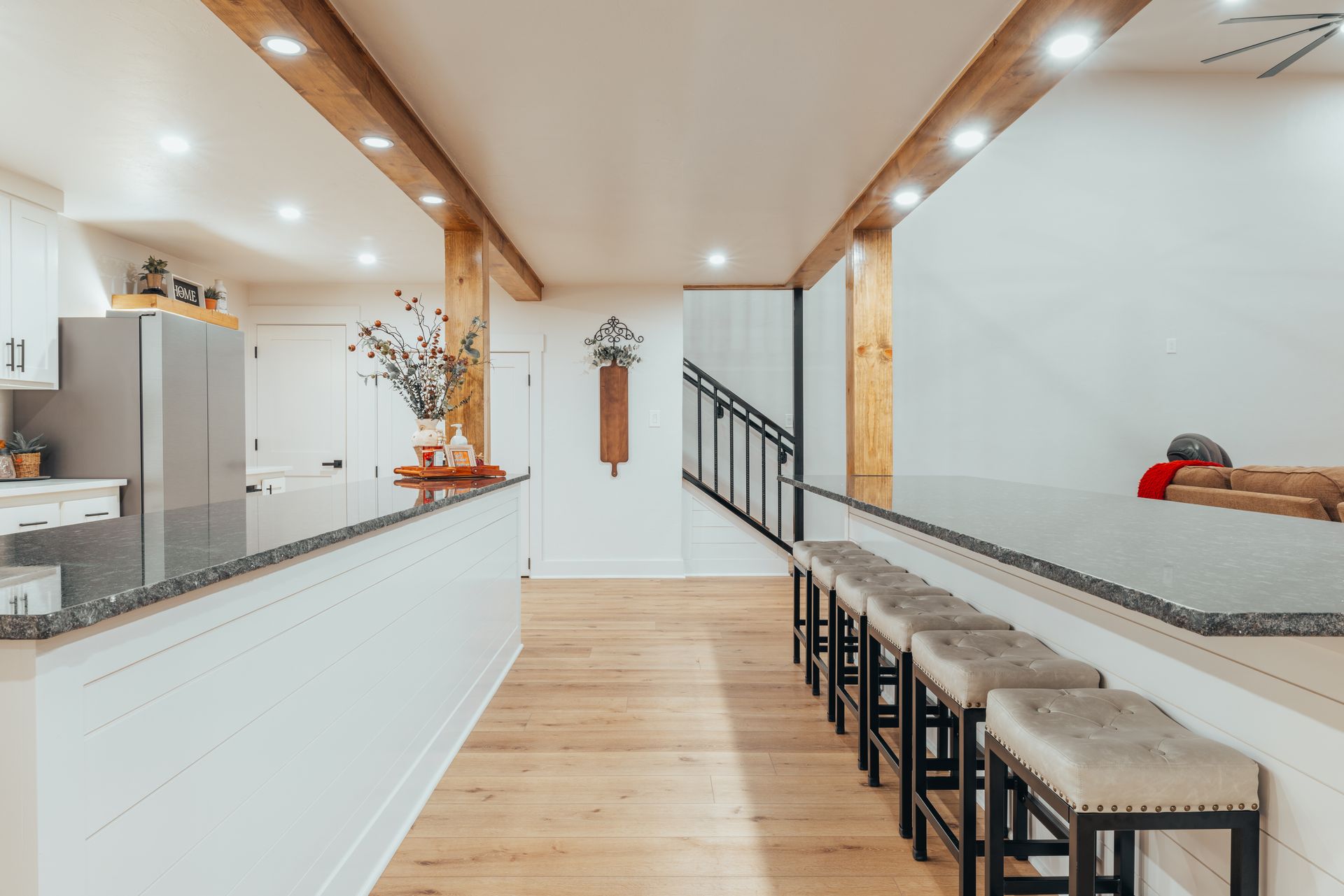 Modern kitchen with a gray countertop, white cabinets, and wooden beams. Bar stools in a row.