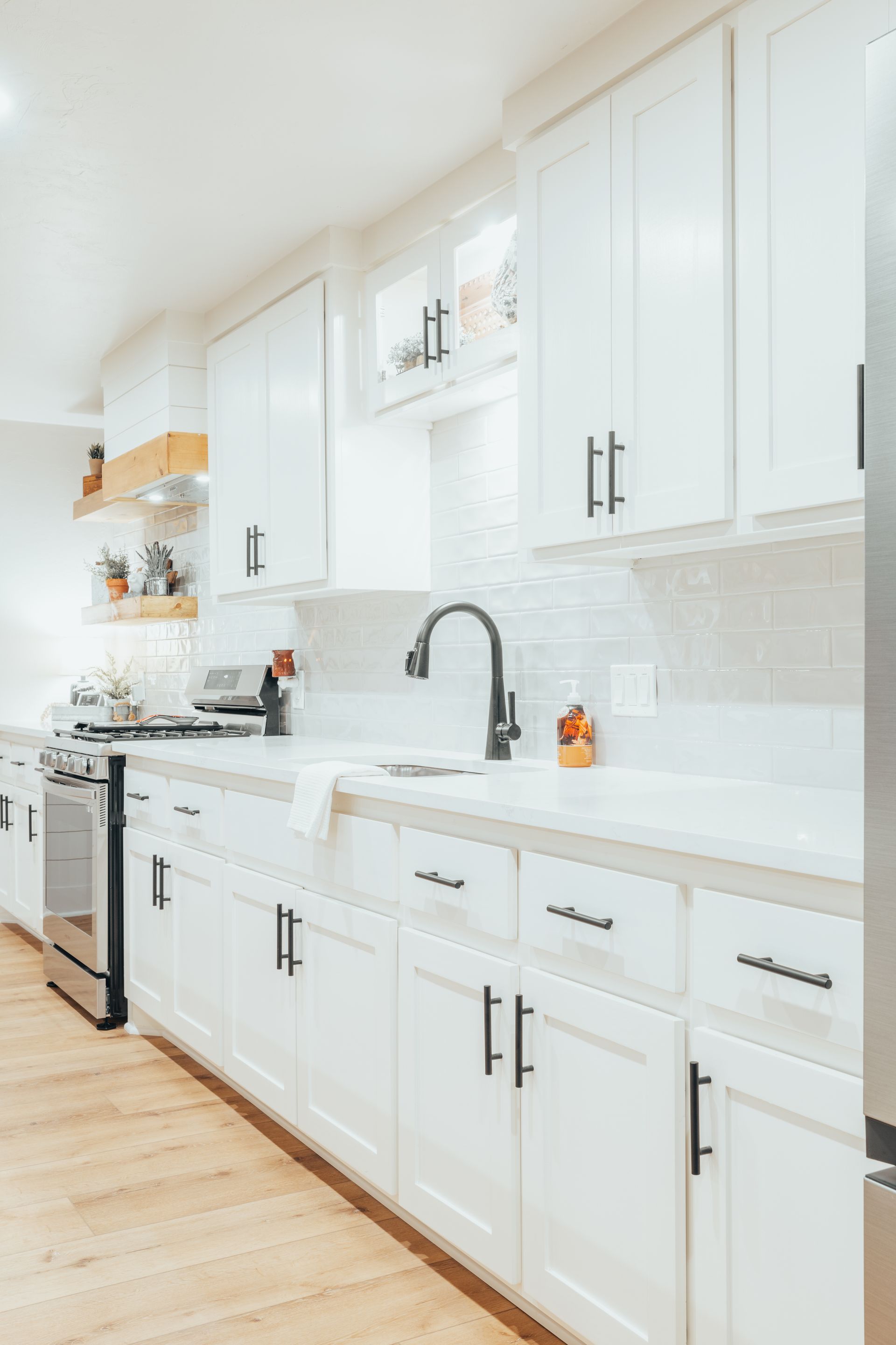 White kitchen with upper and lower cabinets, stainless steel appliances, and black hardware.