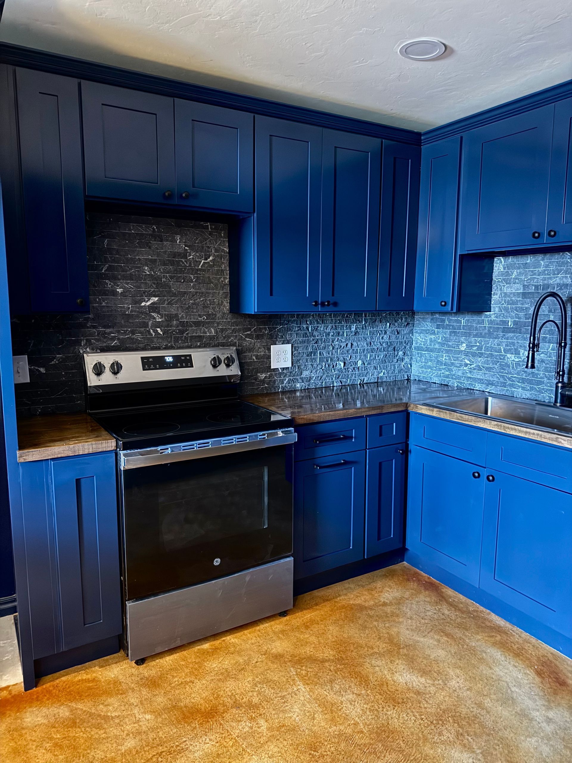 Blue kitchen with dark backsplash, stainless steel appliances, and brown countertops.