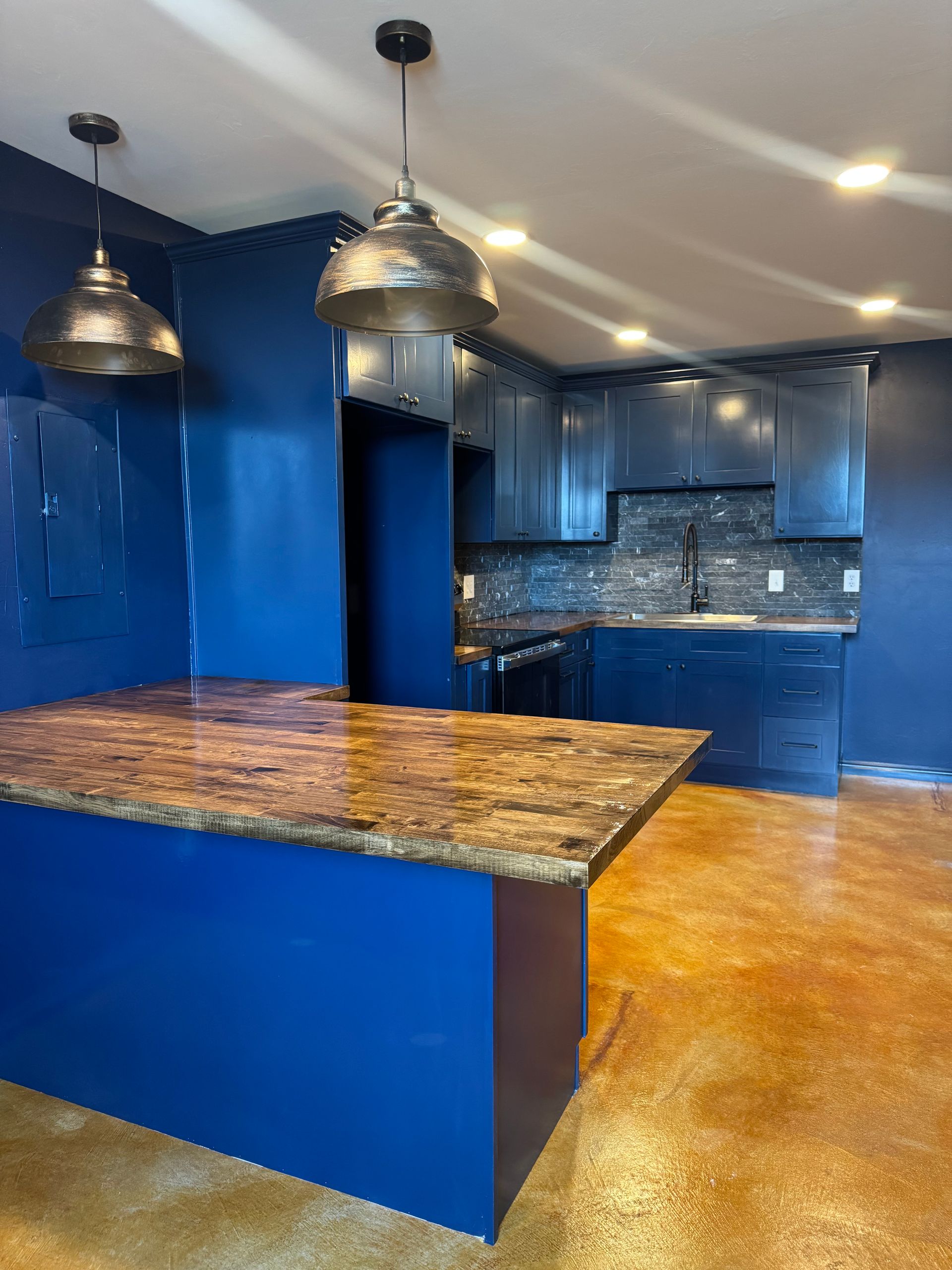 A modern kitchen with dark blue walls, brown countertops, and bronze pendant lights.