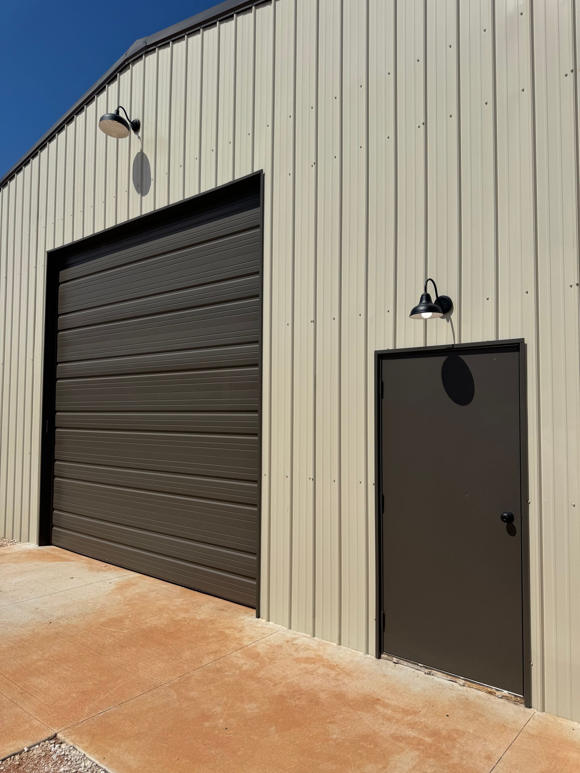 Tan metal building with brown garage door and side door, both with overhead lights.