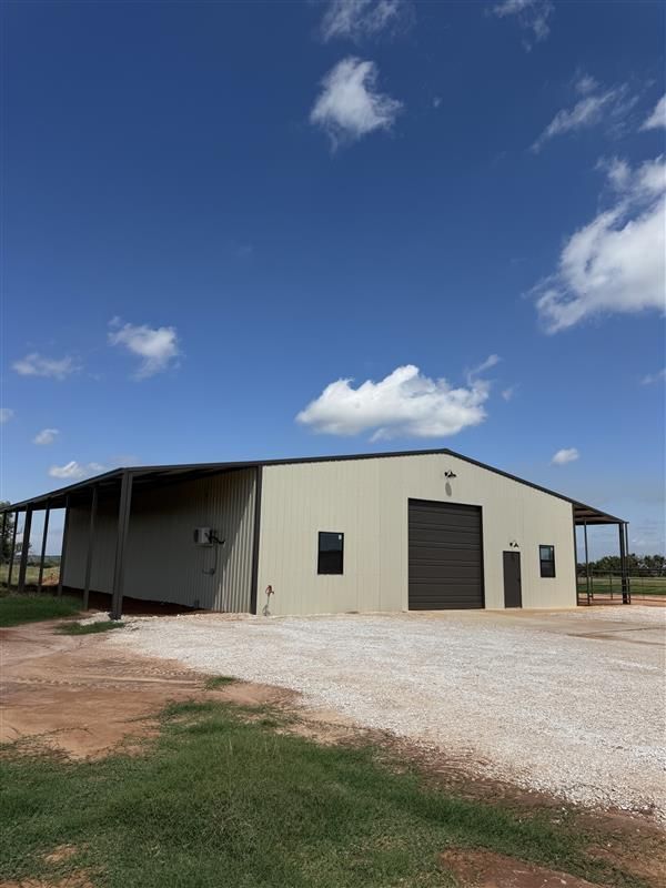 A large metal building with a brown garage door under a blue sky, gravel drive, and green grass.