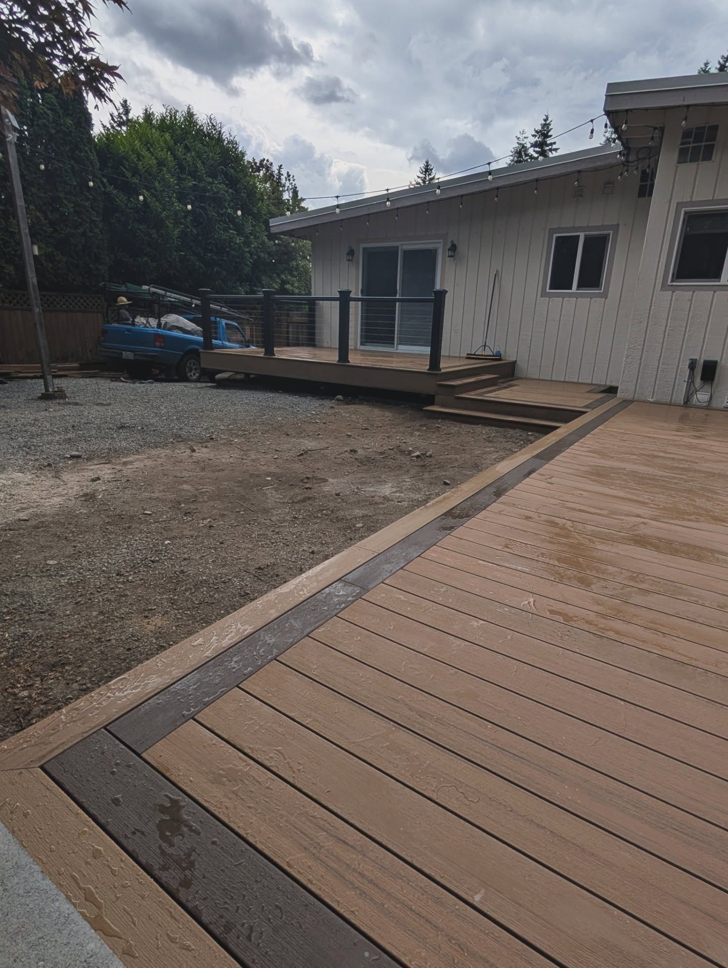 A wooden deck with white house and trees in the background.
