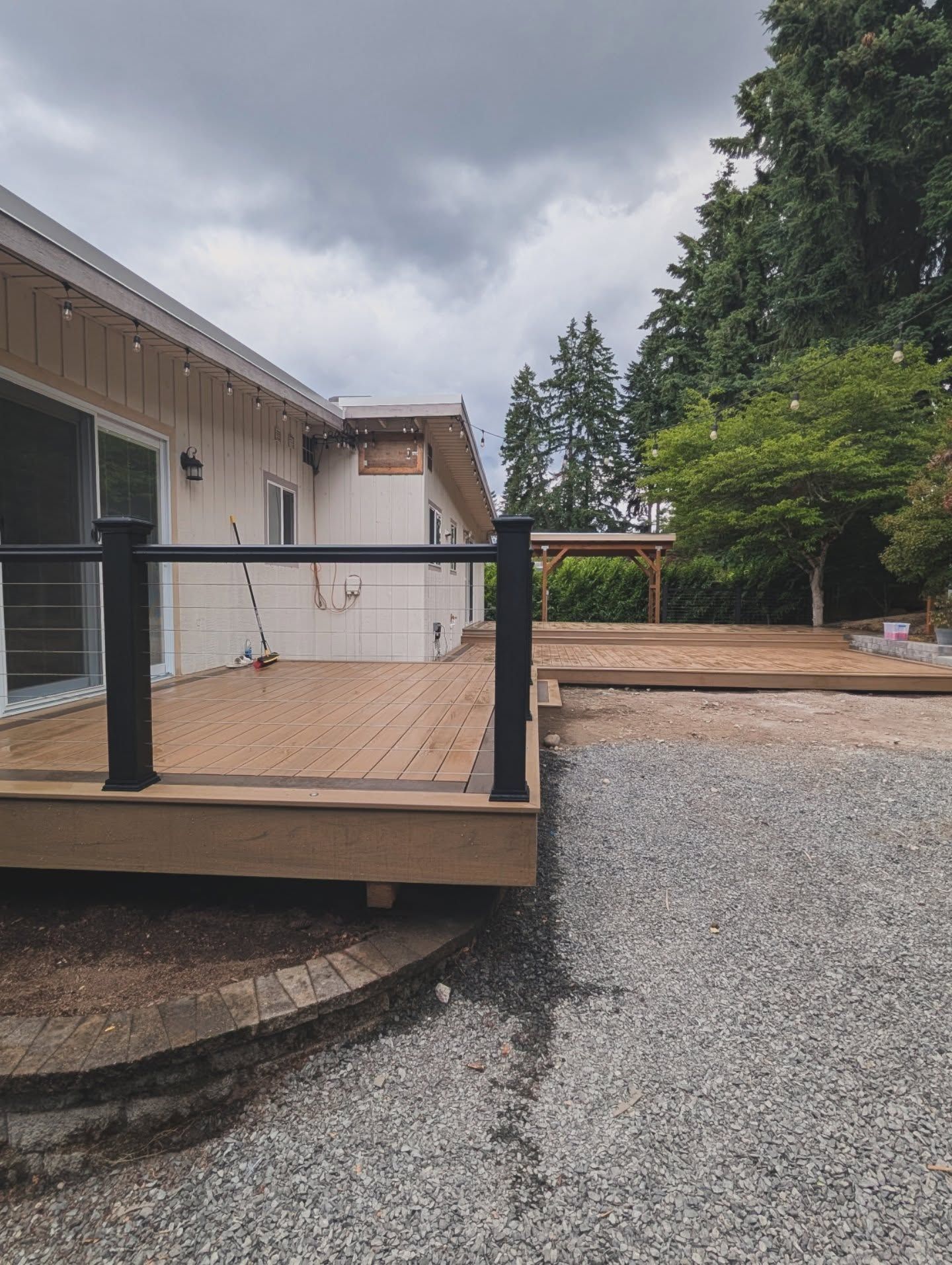 A wooden deck with black railing and white house in background