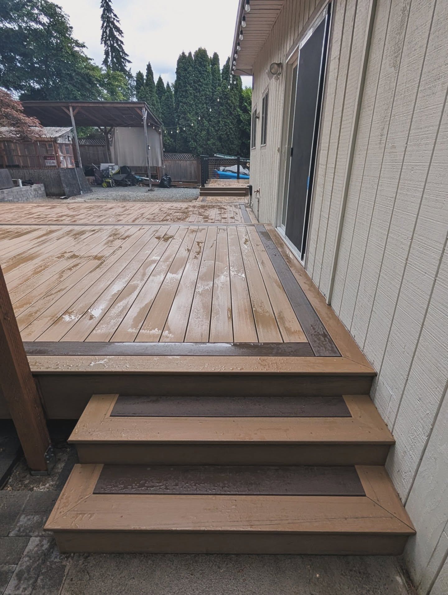 A wooden deck with white house and trees in the background.