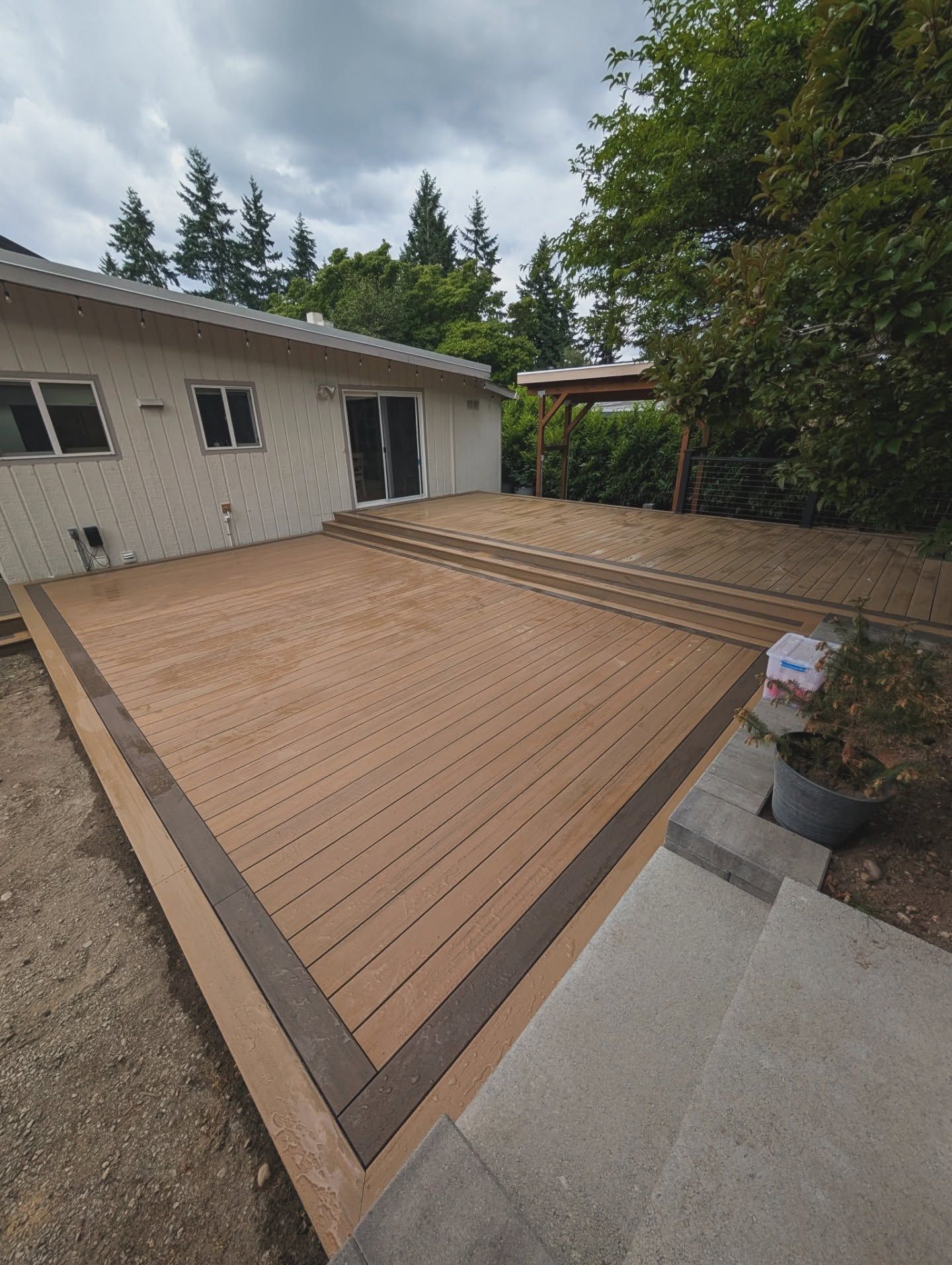 A wooden deck with white house and trees in the background.