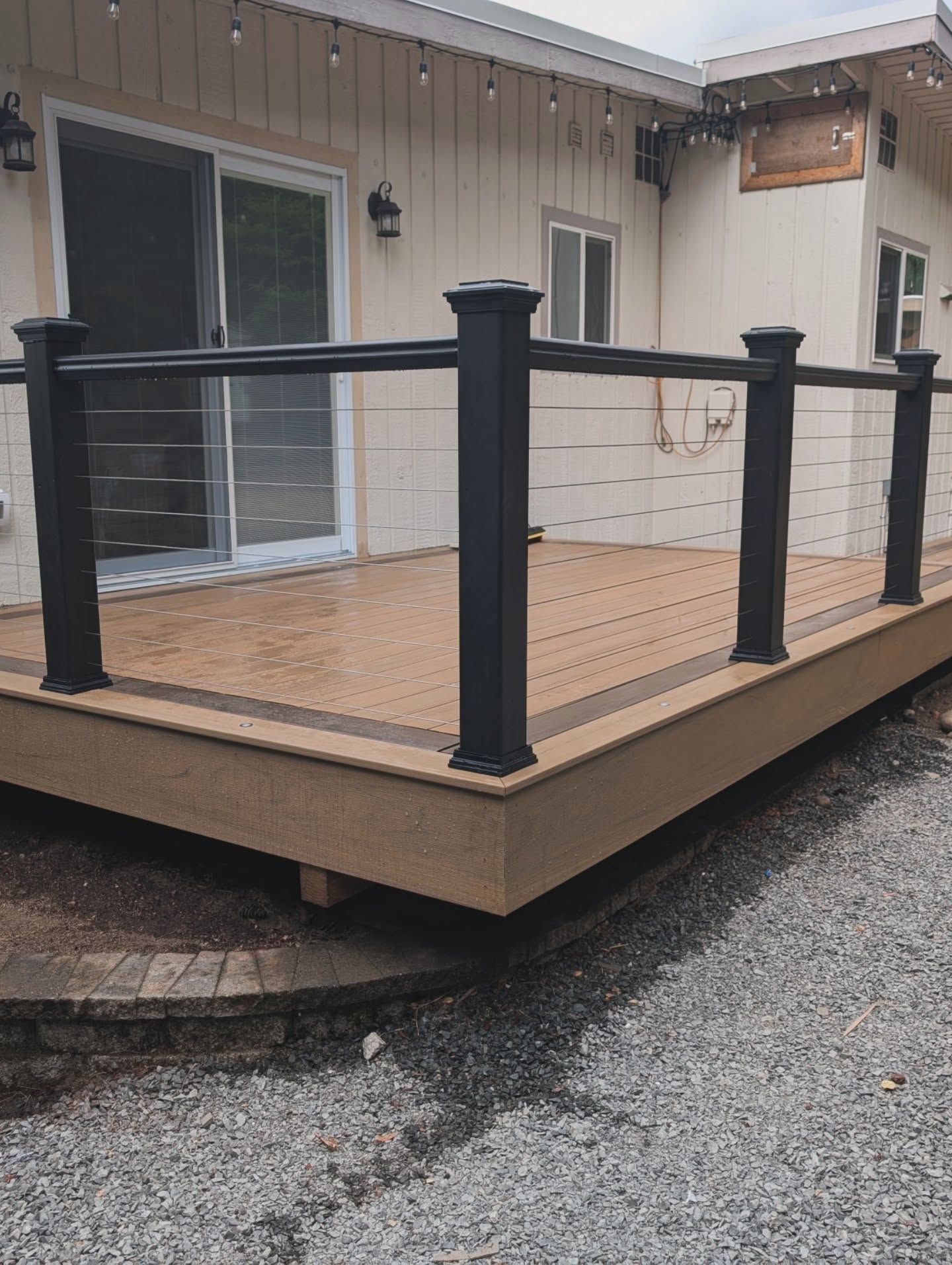 A wooden deck with black railing and white house in background