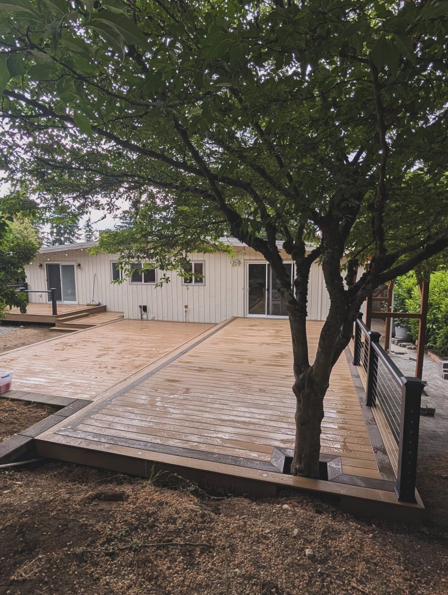 A wooden deck with white house and trees in the background.
