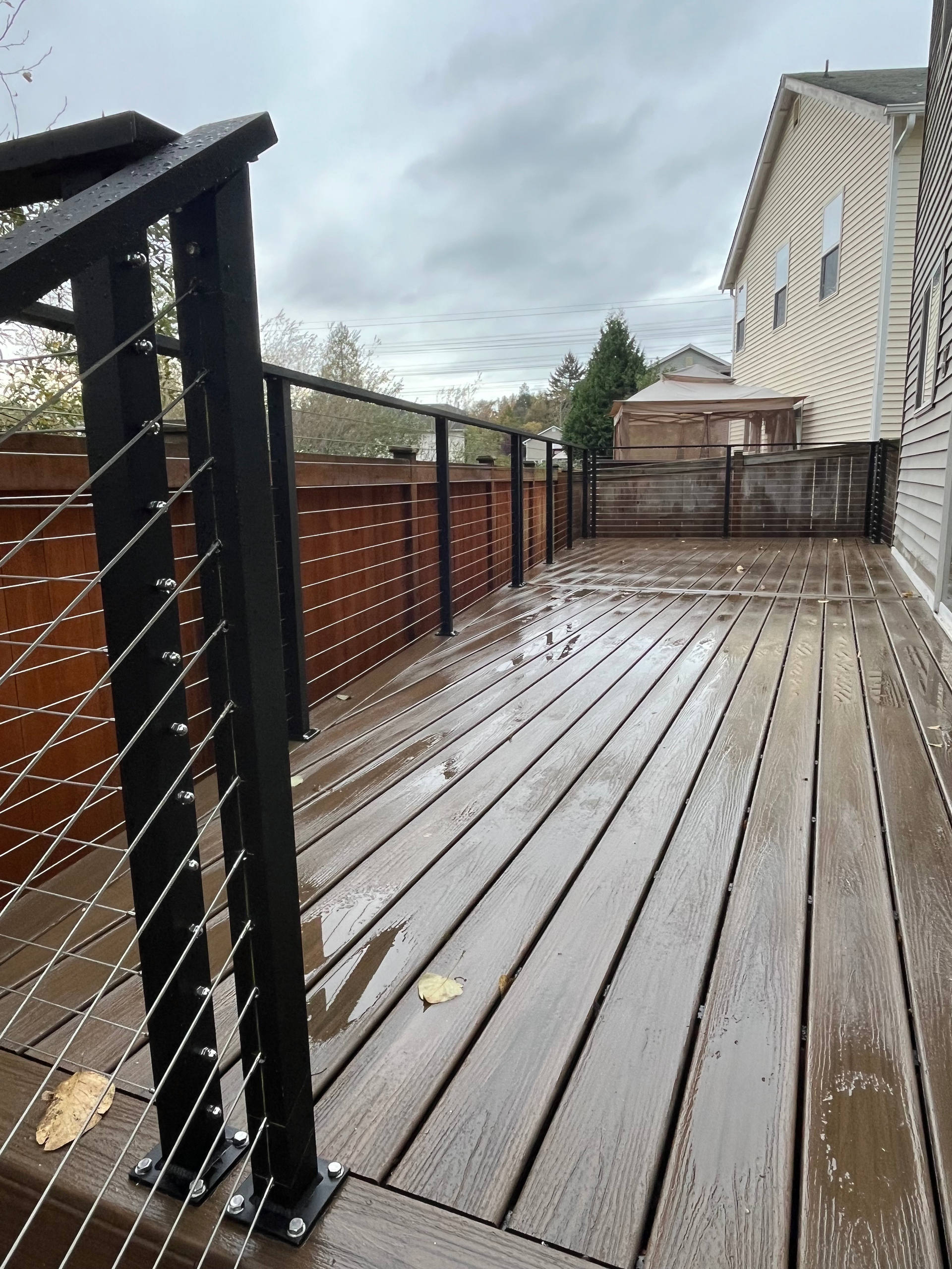 A wooden deck with a black railing and a house in the background.